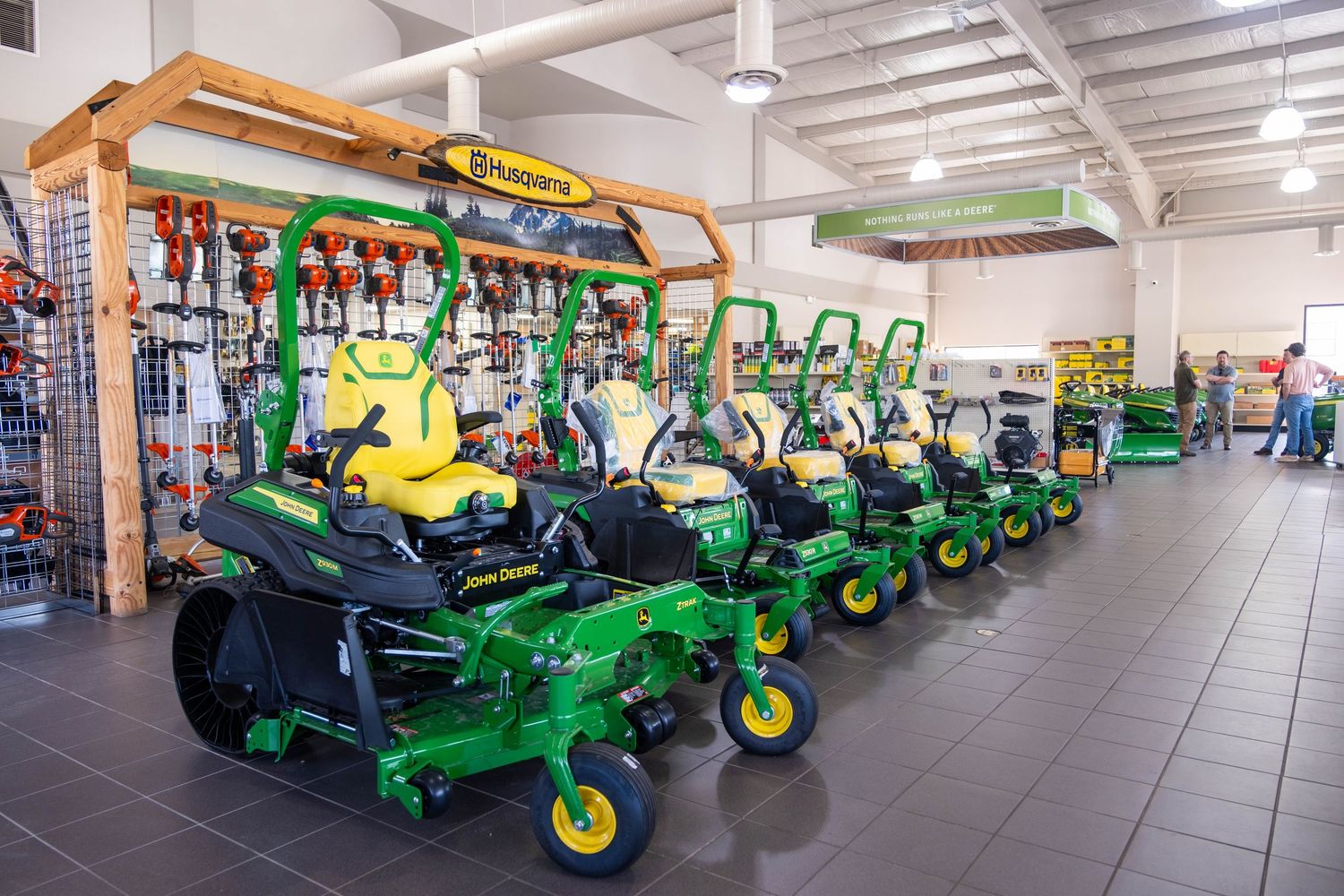 A showroom floor displaying a lineup of John Deere and Husqvarna zero-turn riding lawn mowers.