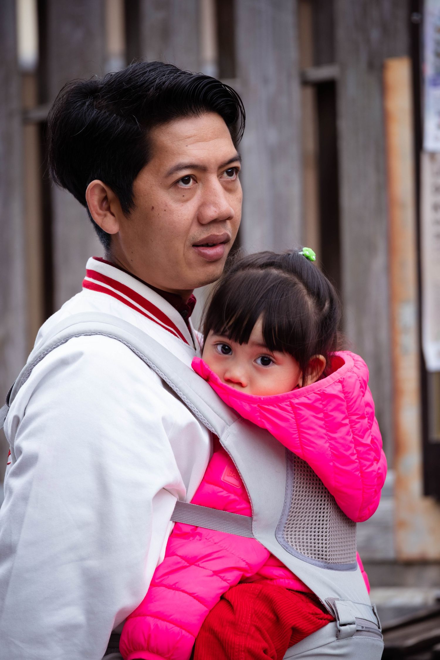 A man carries a young child in a baby carrier on his chest outdoors.
