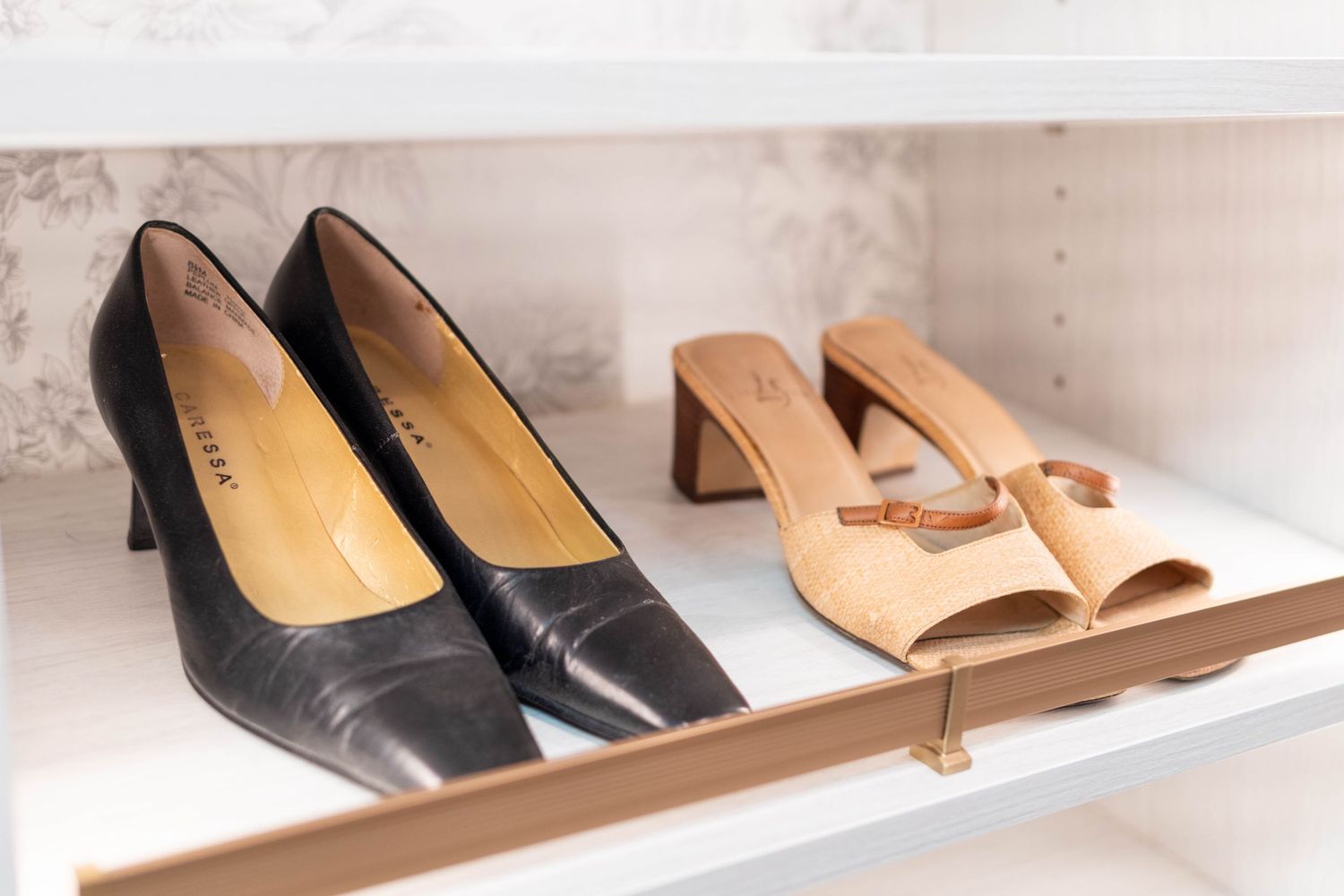 Black kitten heel pumps and tan open-toe mule sandals displayed on a white closet shelf.