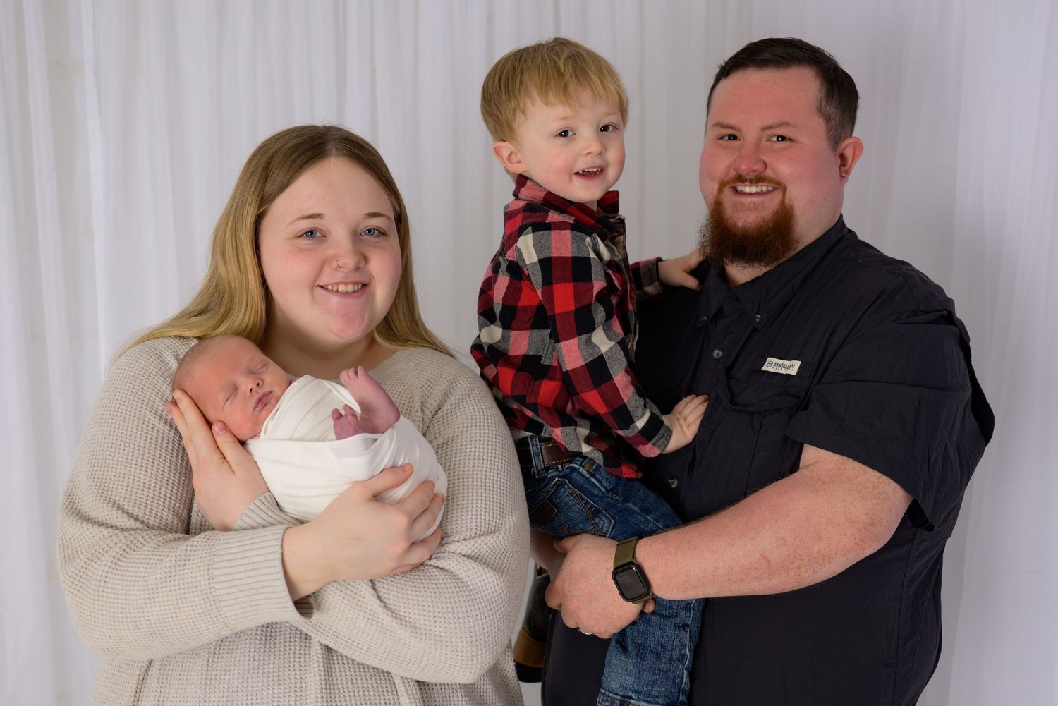 Happy family of four posing for newborn photo session with baby and toddler son.