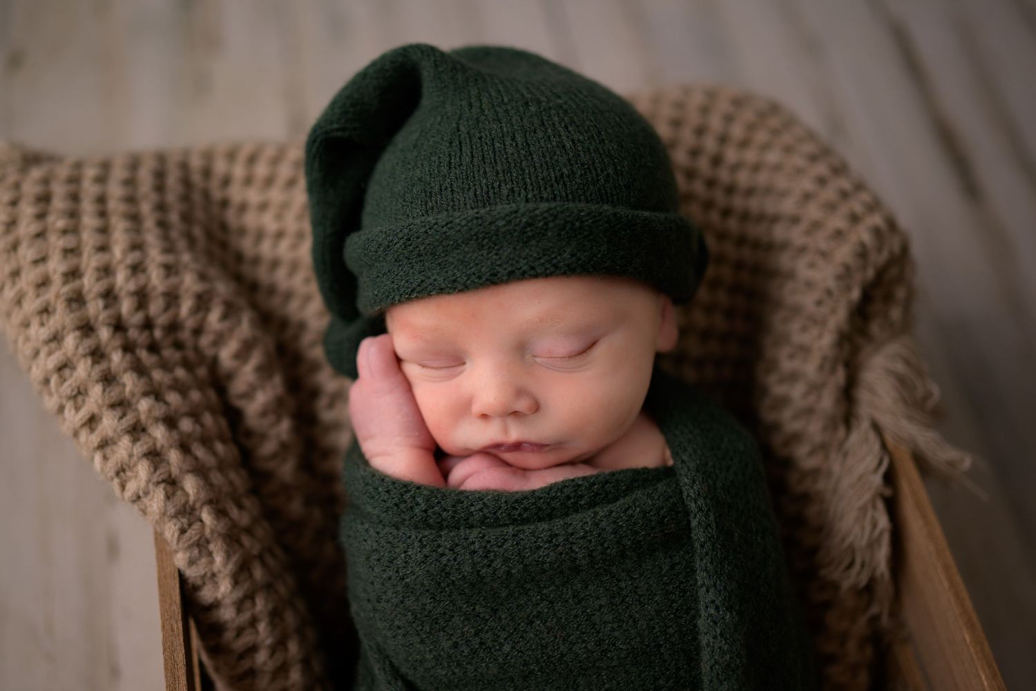 Sleeping newborn baby wrapped in dark green knit swaddle wearing matching sleepy hat.