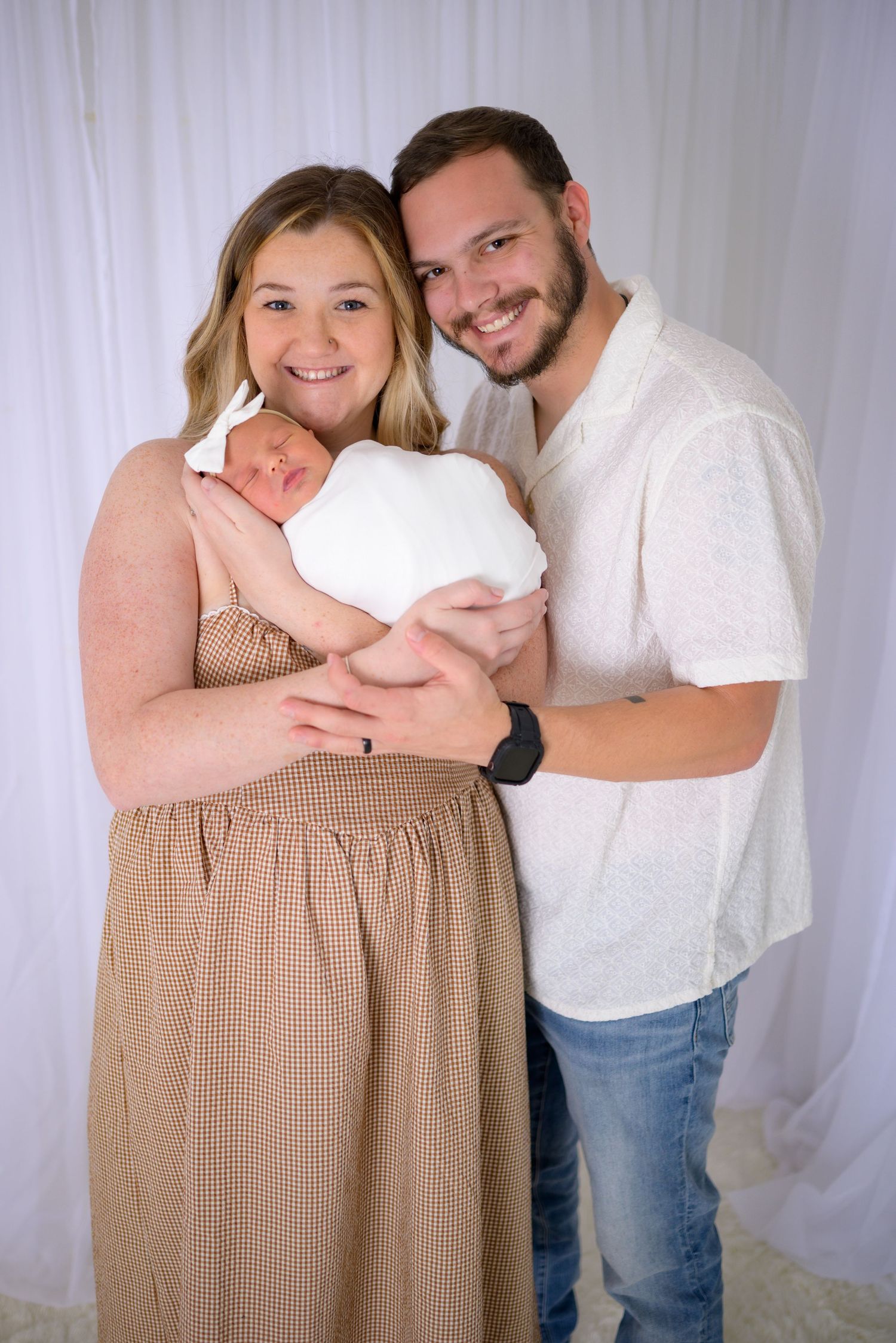 Smiling new parents holding swaddled newborn baby during professional newborn photography session.