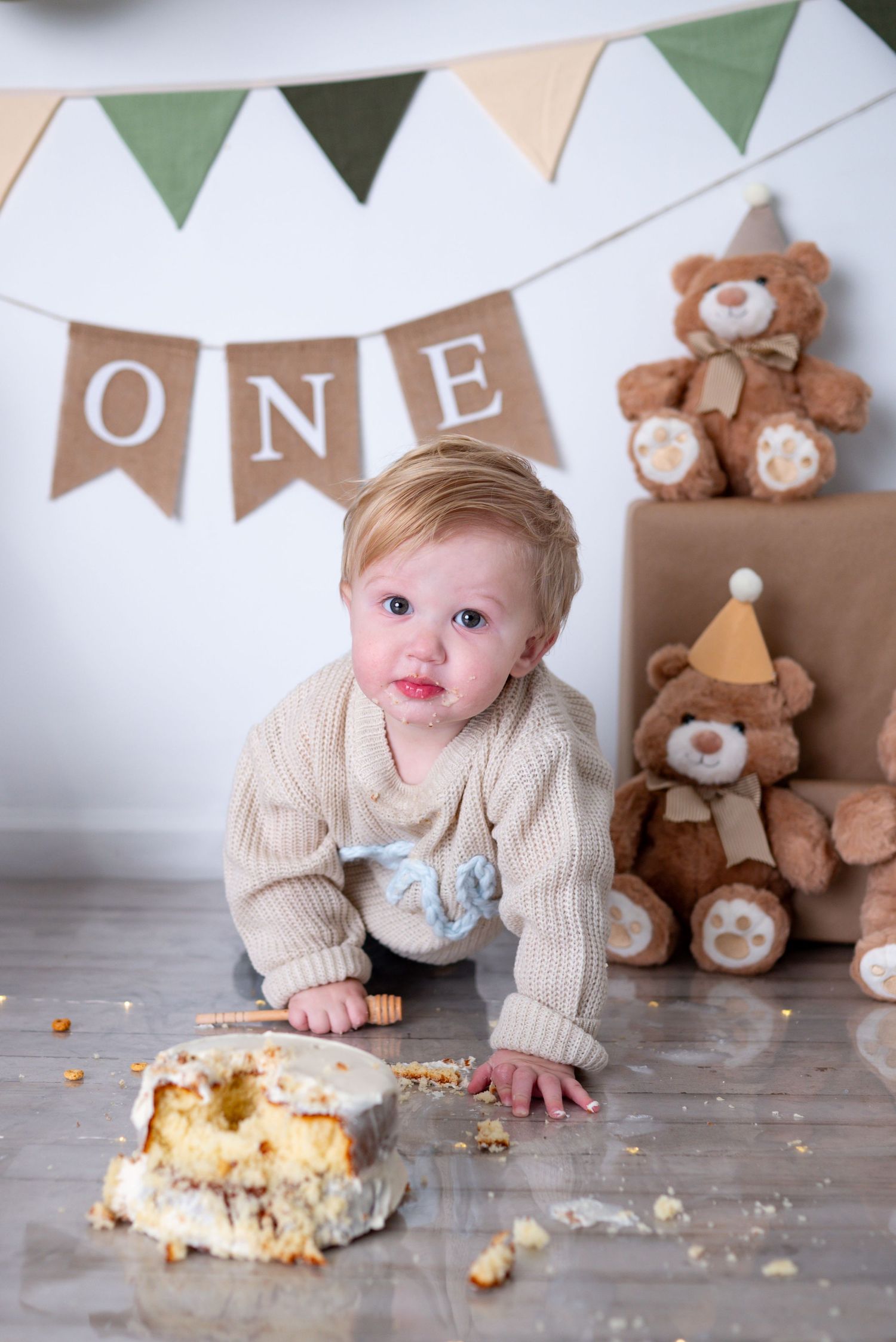 Baby boy crawls toward demolished smash cake during first birthday photoshoot with teddy bear decor.