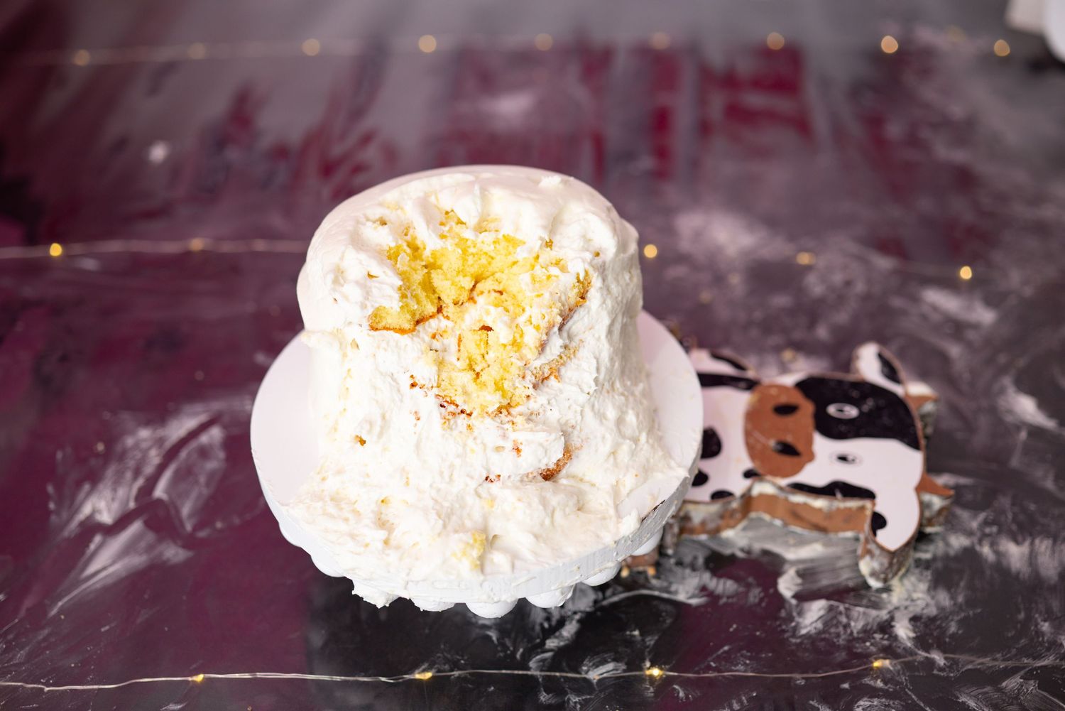 White frosted smash cake with yellow cake visible on top sits on white plate for first birthday.