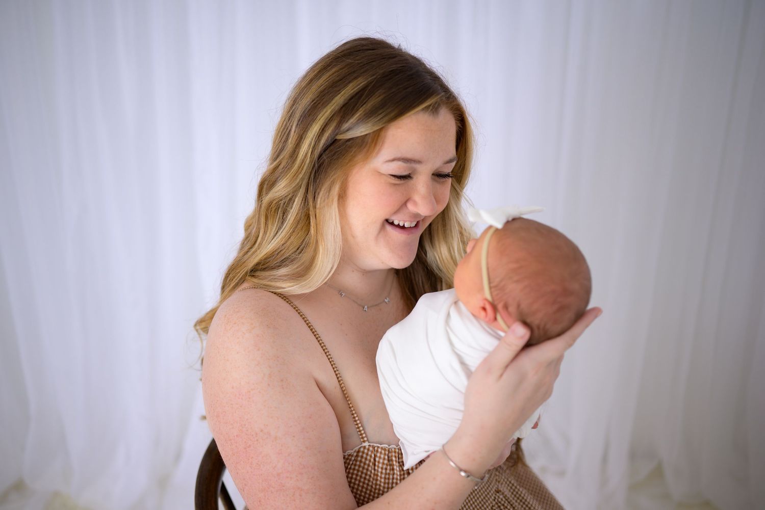 Happy young mother smiling joyfully while cradling her sleeping white-swaddled newborn baby.