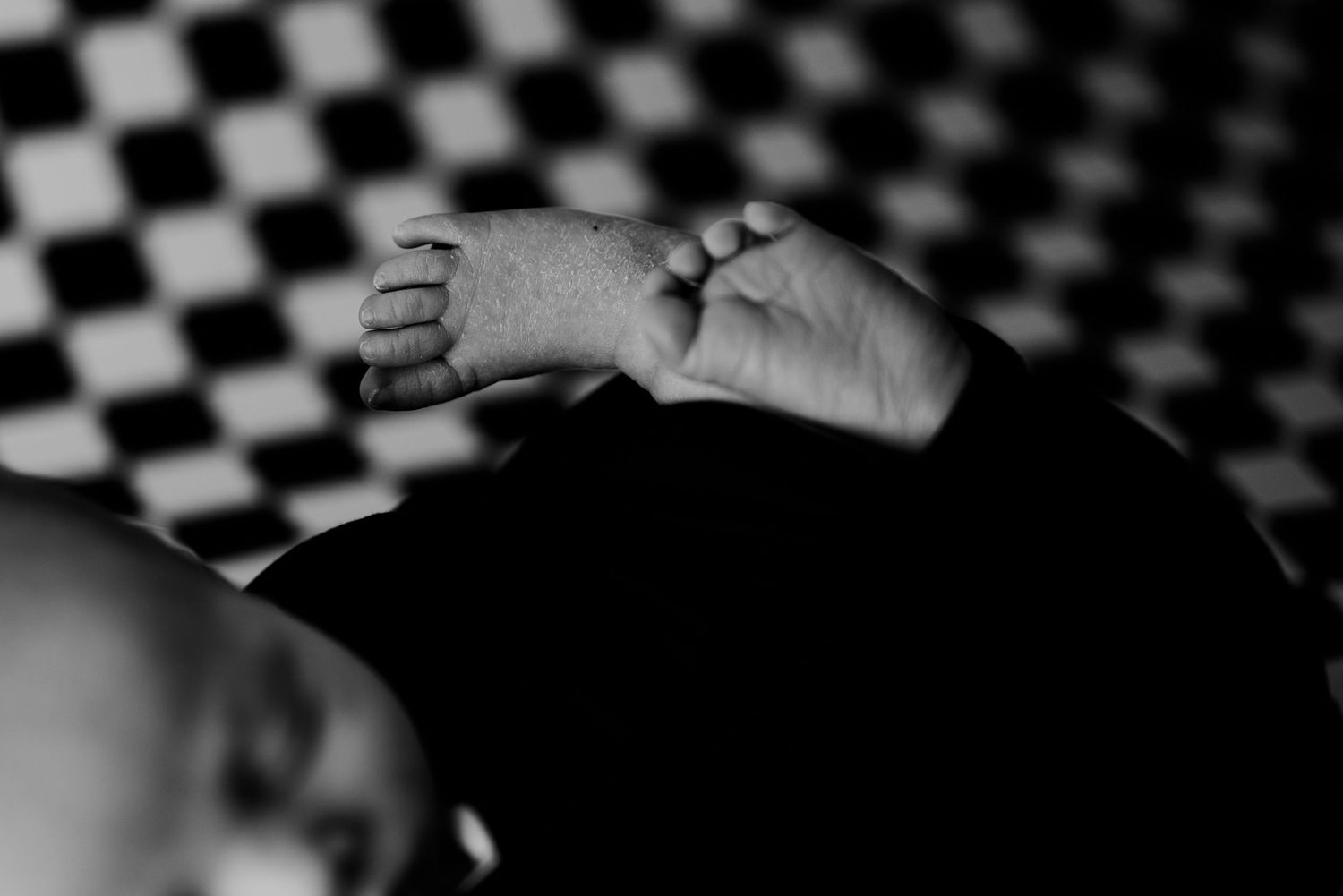 Black and white photo of newborn baby feet and hands on checkered backdrop.