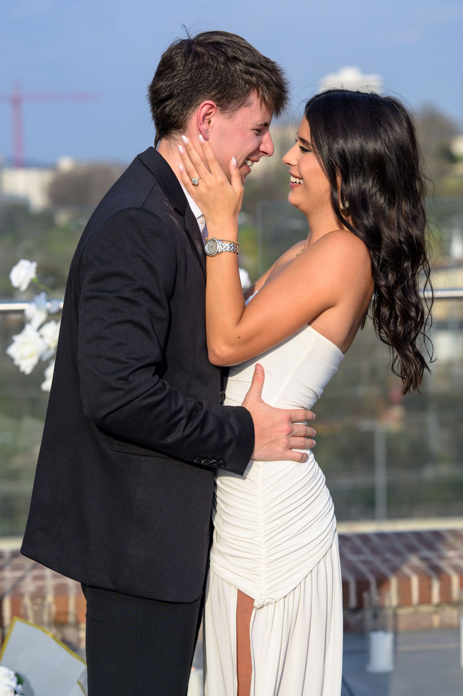 Happy couple embracing and smiling on rooftop with Nashville skyline and white floral arrangements.