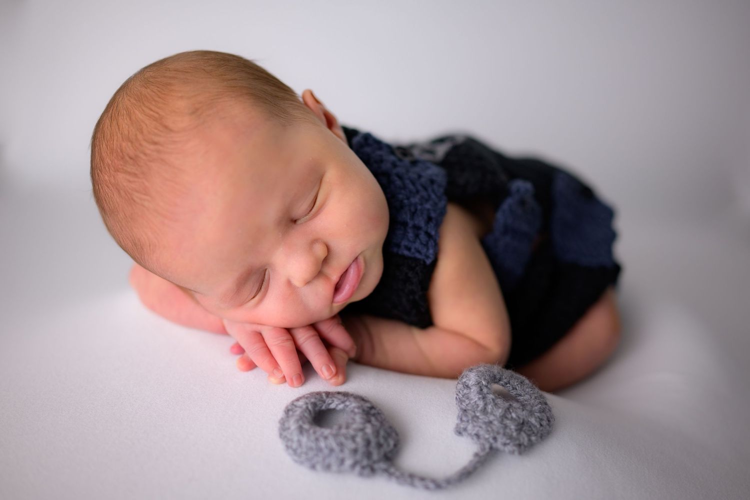 Sleeping newborn baby boy posed in navy blue knit outfit with matching booties.
