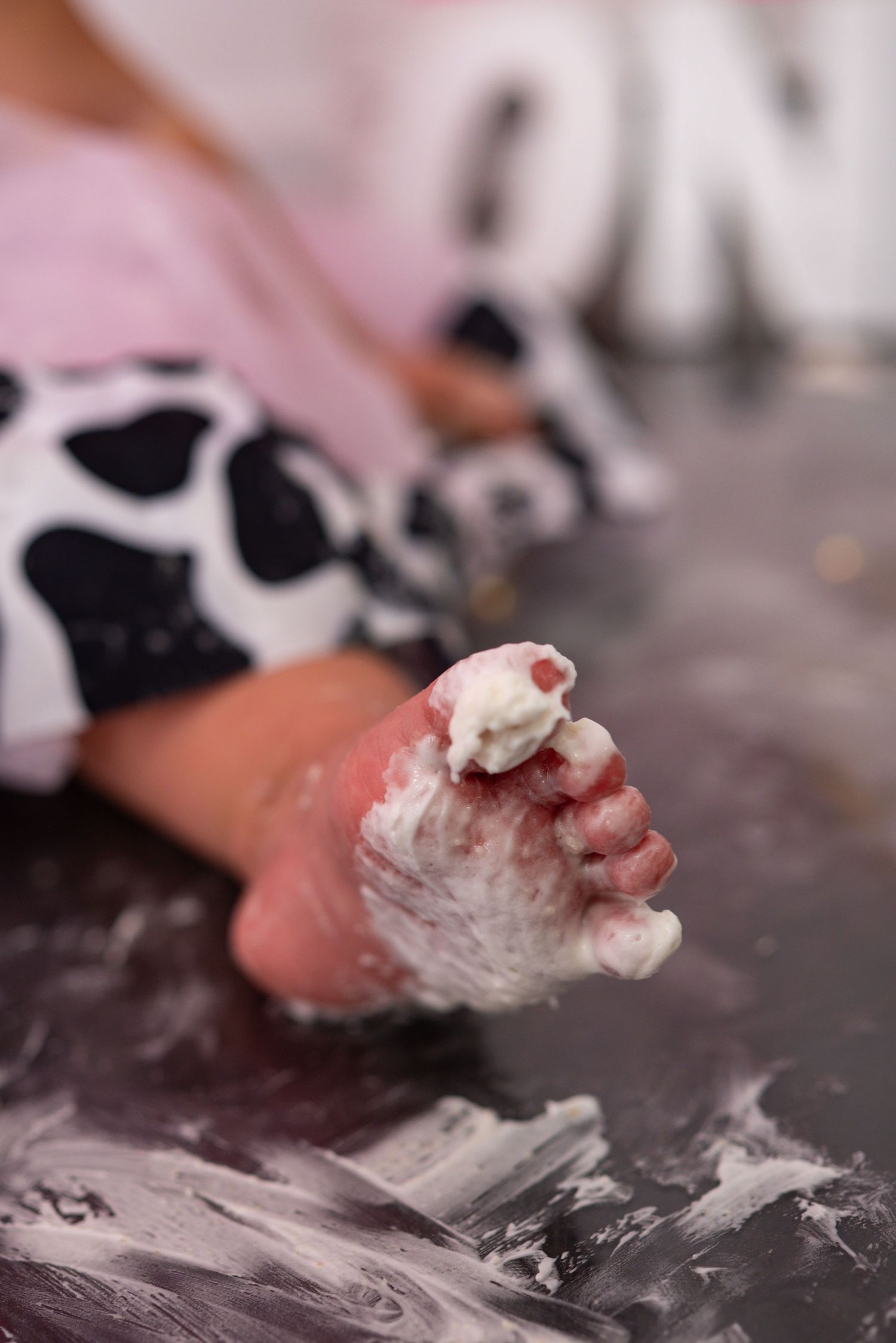 Close-up of baby foot covered in white cake frosting during first birthday cake smash.