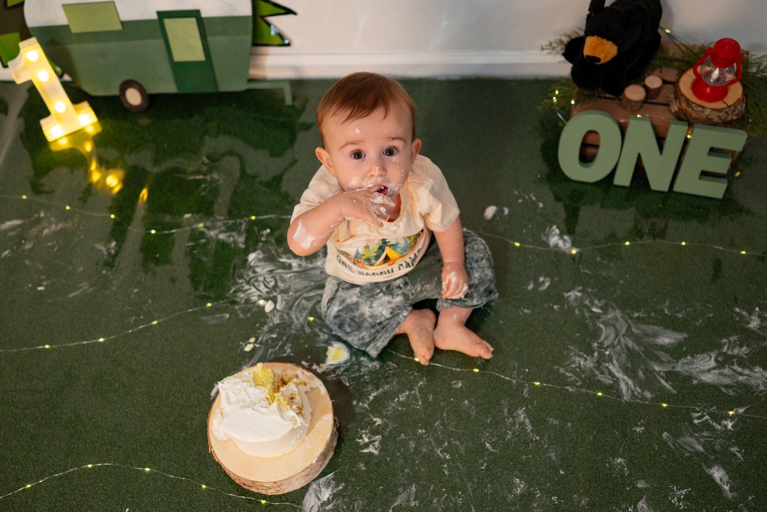 Overhead view of baby eating smash cake surrounded by camping decor at his first birthday cake smash session.
