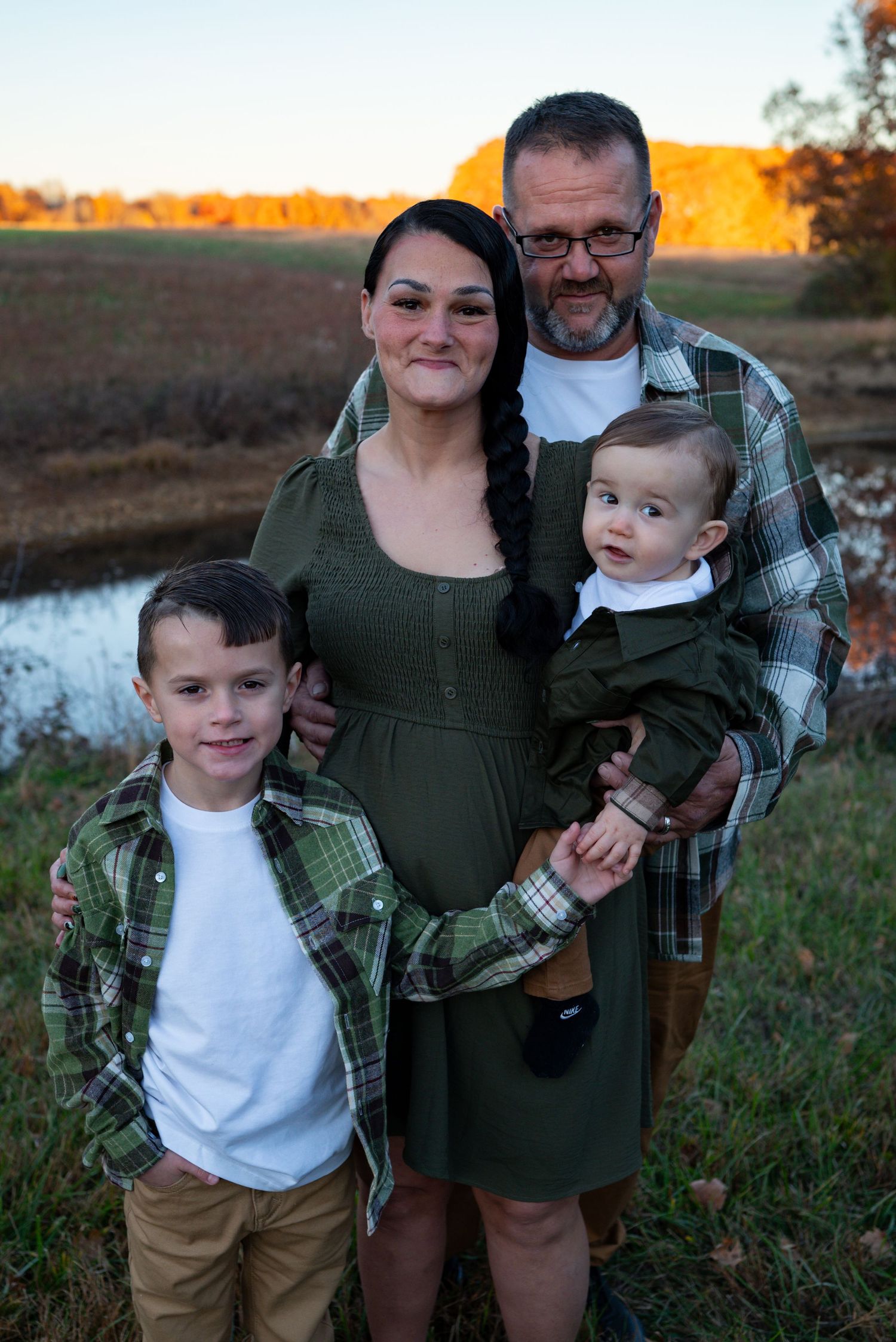 Family of four posing near autumn pond at sunset, wearing coordinating green and plaid outfits.