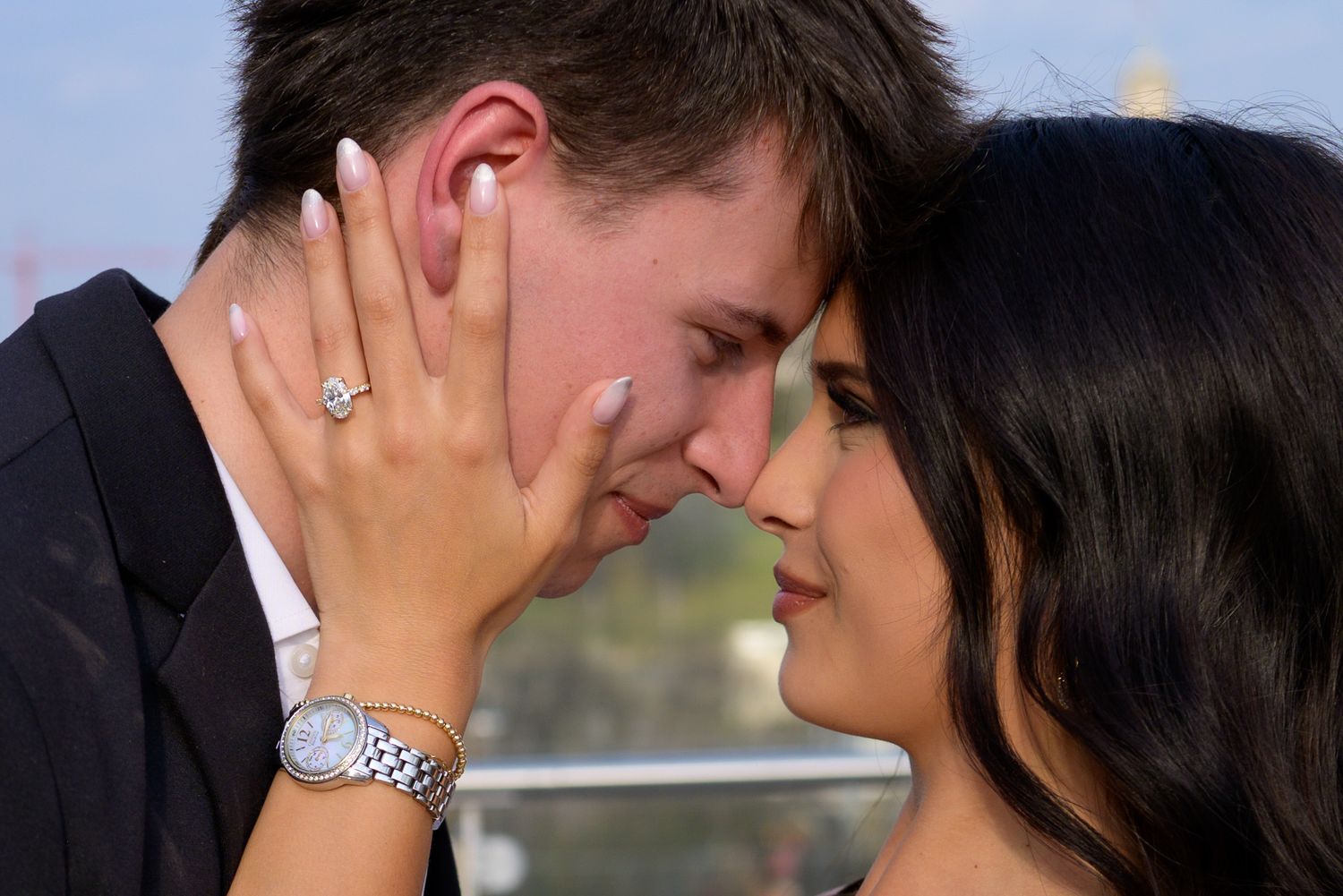 Close-up of couple touching foreheads showing engagement ring and watch during outdoor proposal.