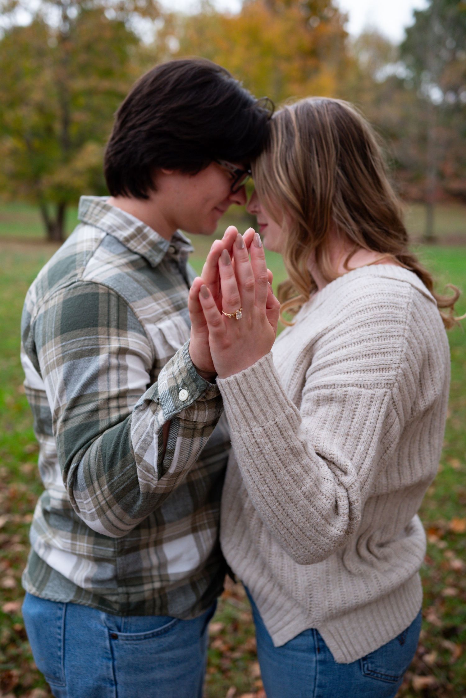 Romantic couple pressing foreheads together with hands clasped in prayer pose in an autumn field for engagement photos.