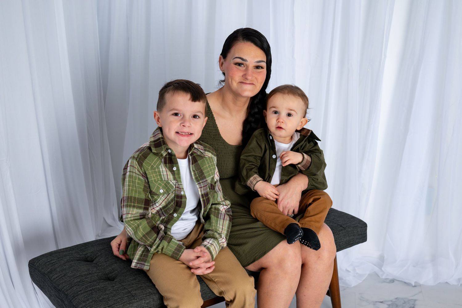 Mother in green dress sits with two young sons in coordinating outfits for a studio family portrait.
