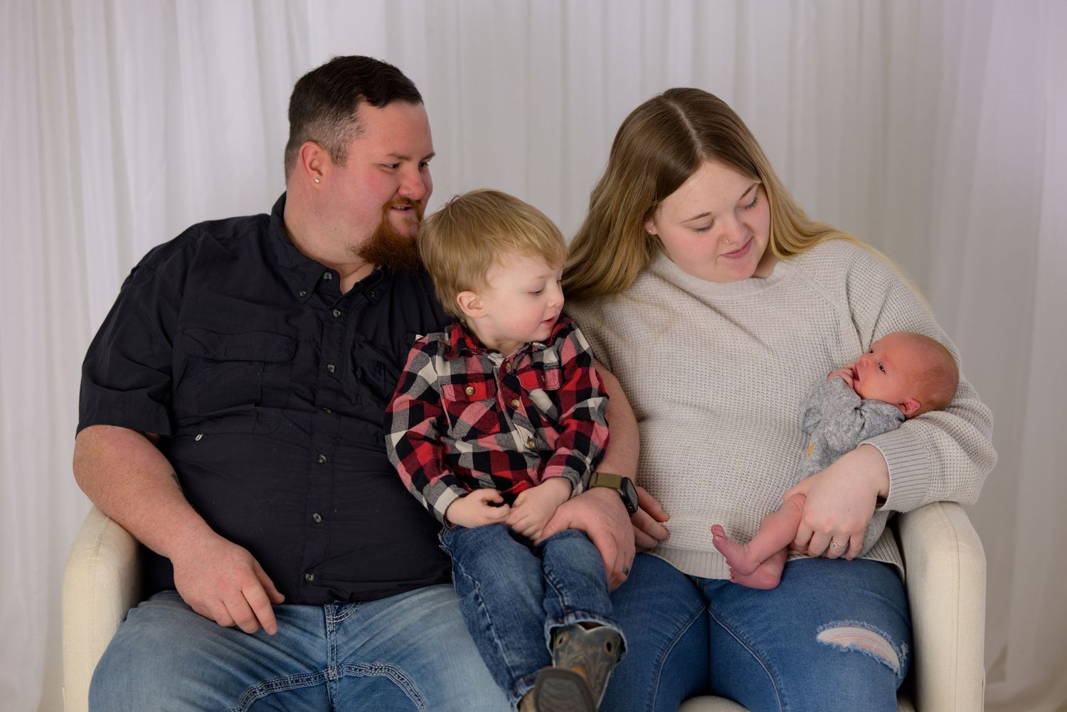 Happy family of four posing together, parents with toddler son and newborn baby during professional photo session.