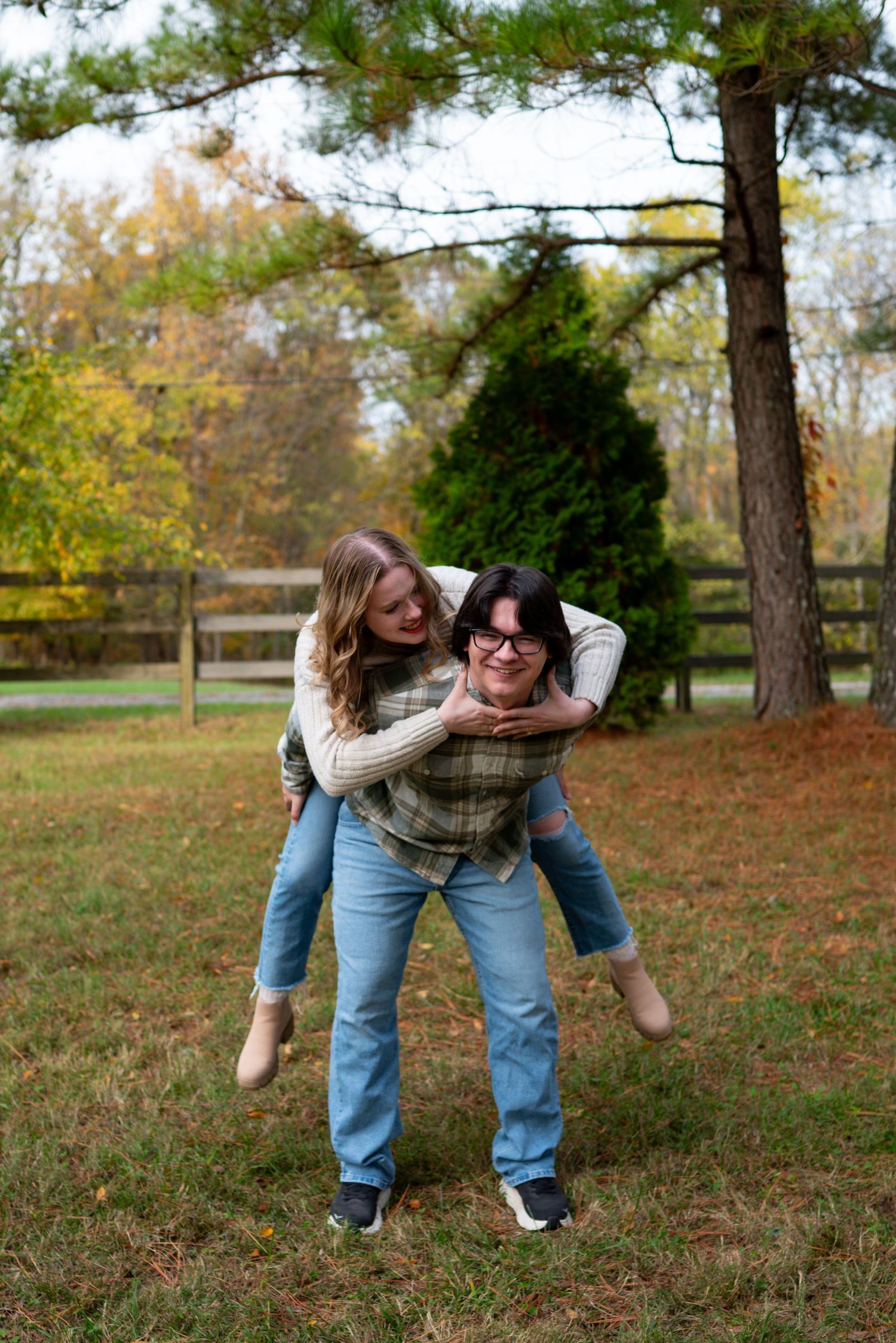 Playful couple laughing as man gives woman a piggyback ride in a colorful autumn field.