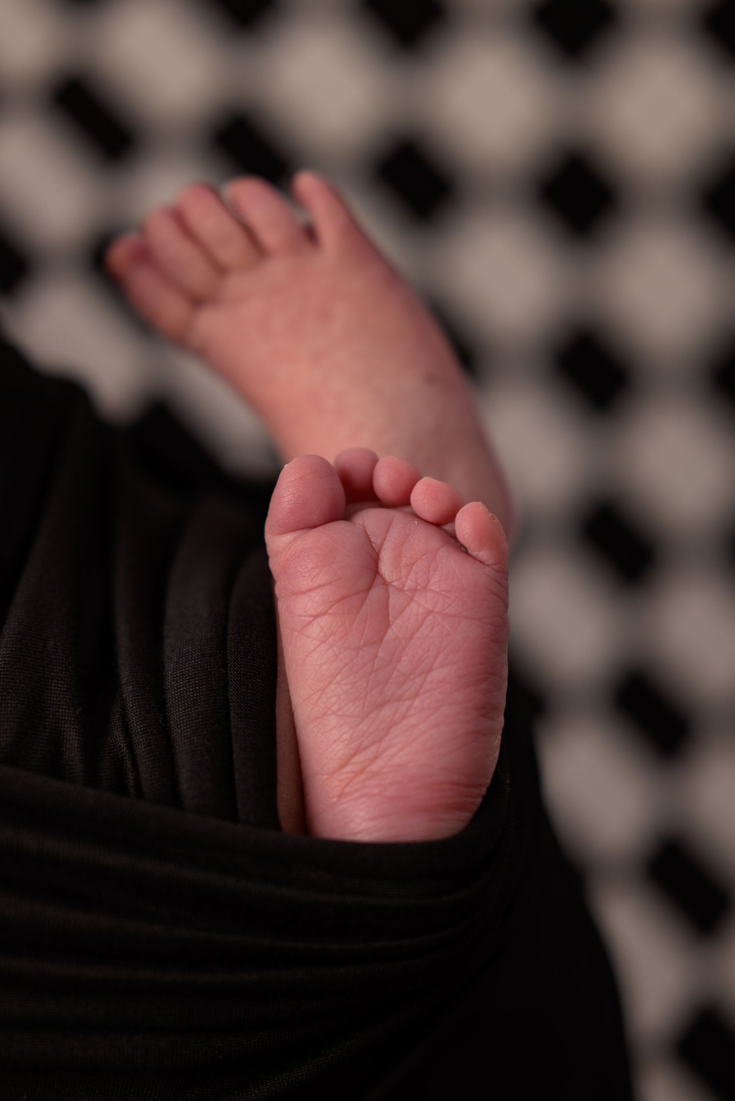 Close-up of tiny newborn baby feet peeking out from black swaddle wrap.