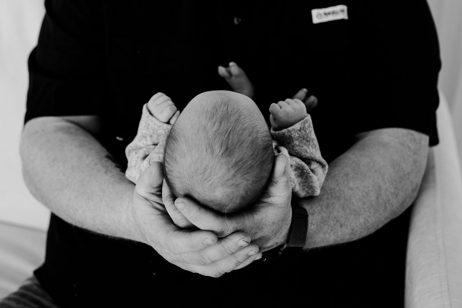 Black and white photo of father cradling curled newborn baby in his hands.