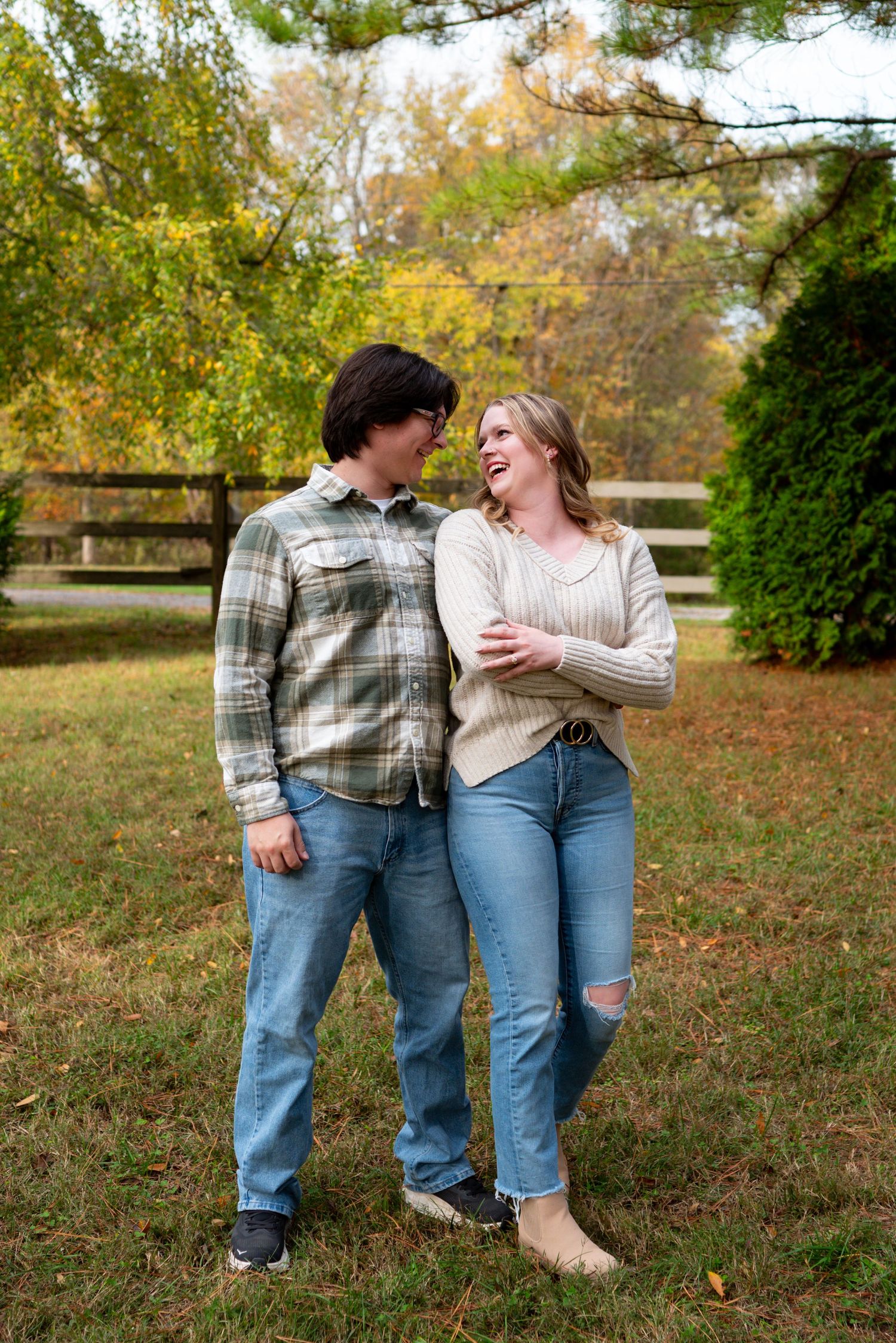 Young couple laughing together while standing arm in arm in a lush autumn field setting.