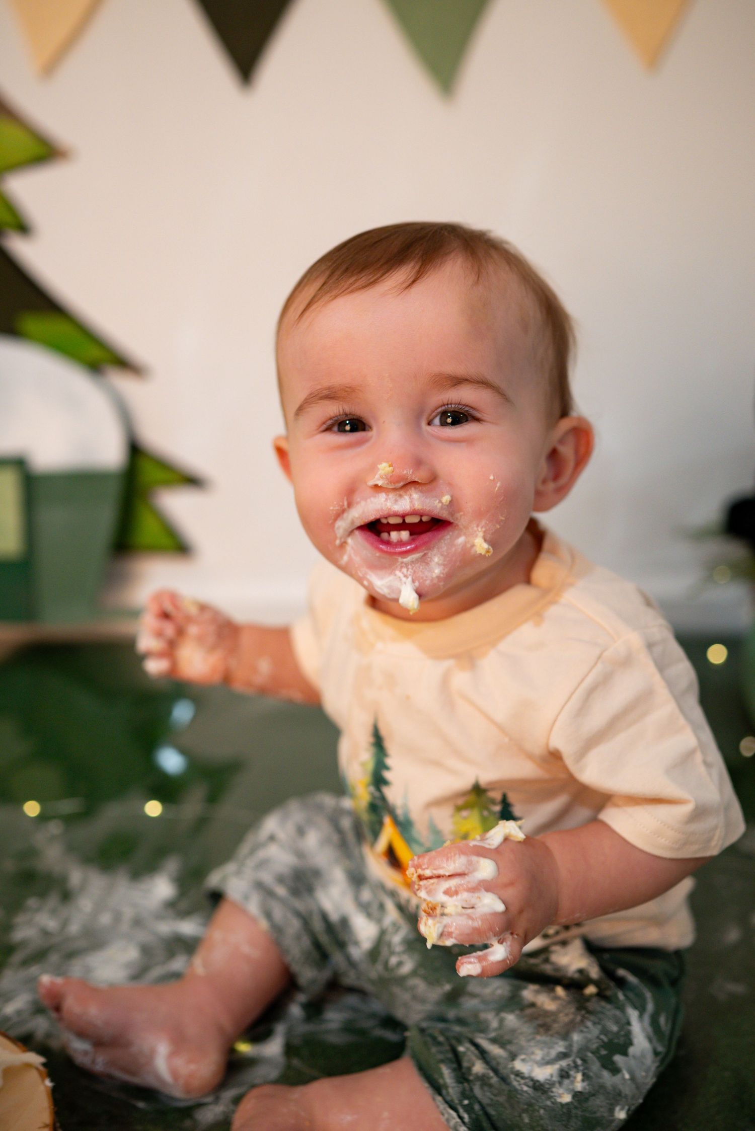 Happy frosting-covered baby laughs during his camping-themed first birthday cake smash photoshoot.