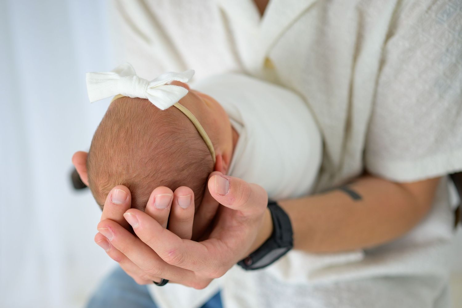 Close-up of parents hands cradling sleeping newborn baby with white bow headband.