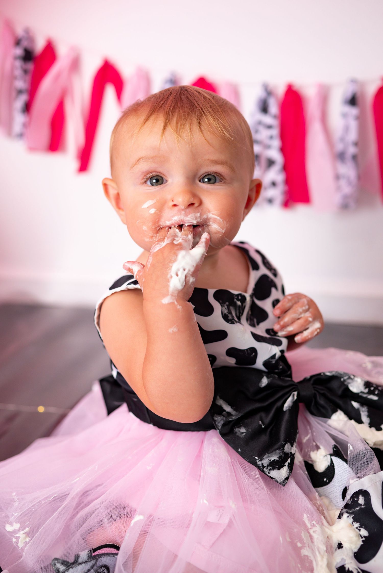 Baby girl with cake frosting on face enjoys messy first birthday cake smash photoshoot.