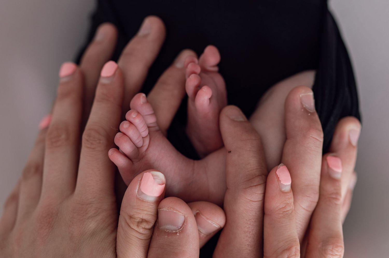 Adult hands cradling tiny newborn baby feet, a tender family moment captured in soft natural light.