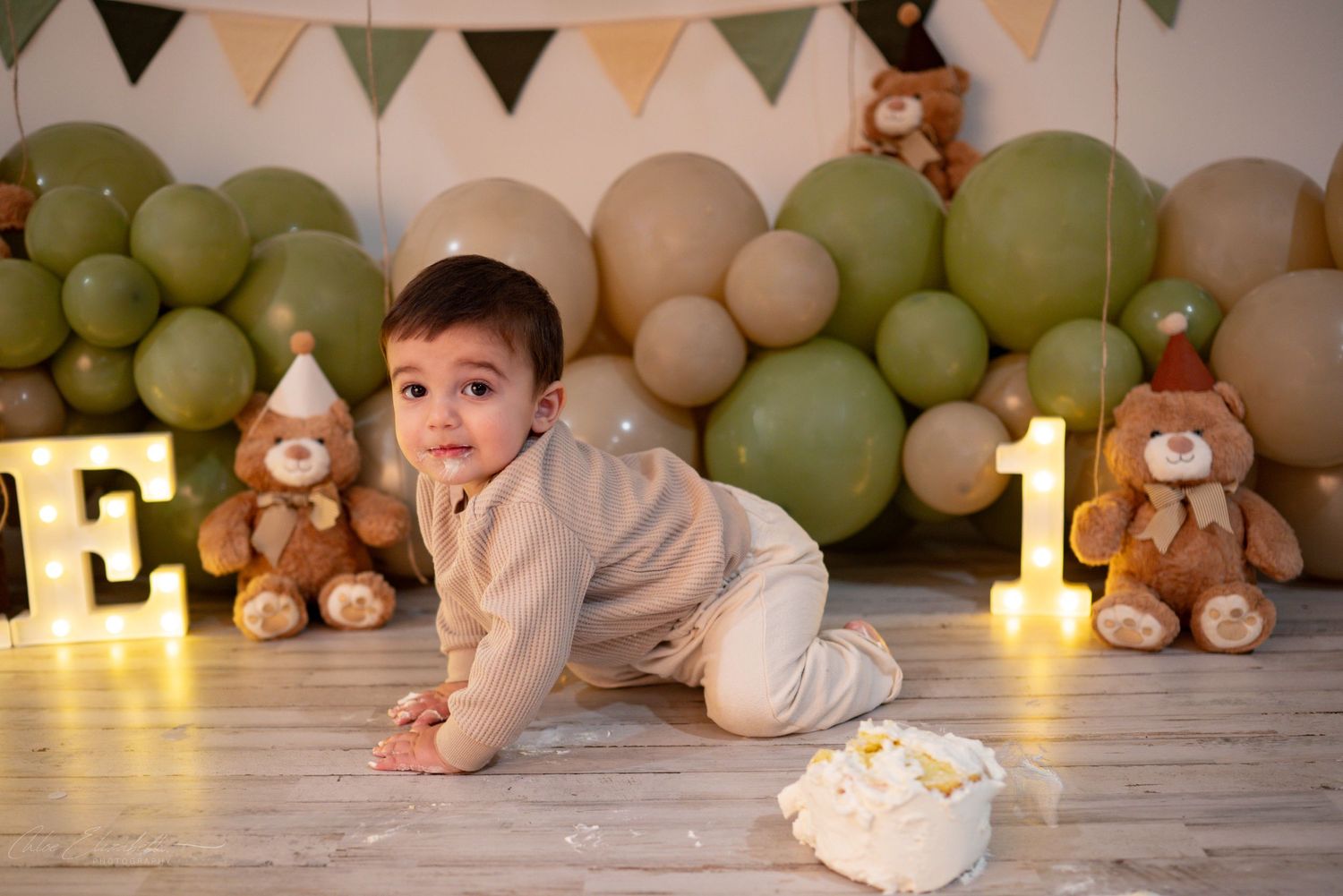 Curious baby boy crawling toward camera at teddy bear themed first birthday cake smash.