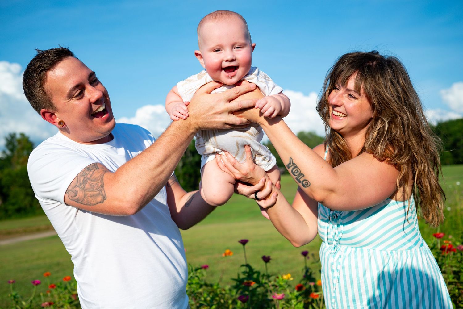 Happy family outdoors lifting laughing baby in sunny flower garden.