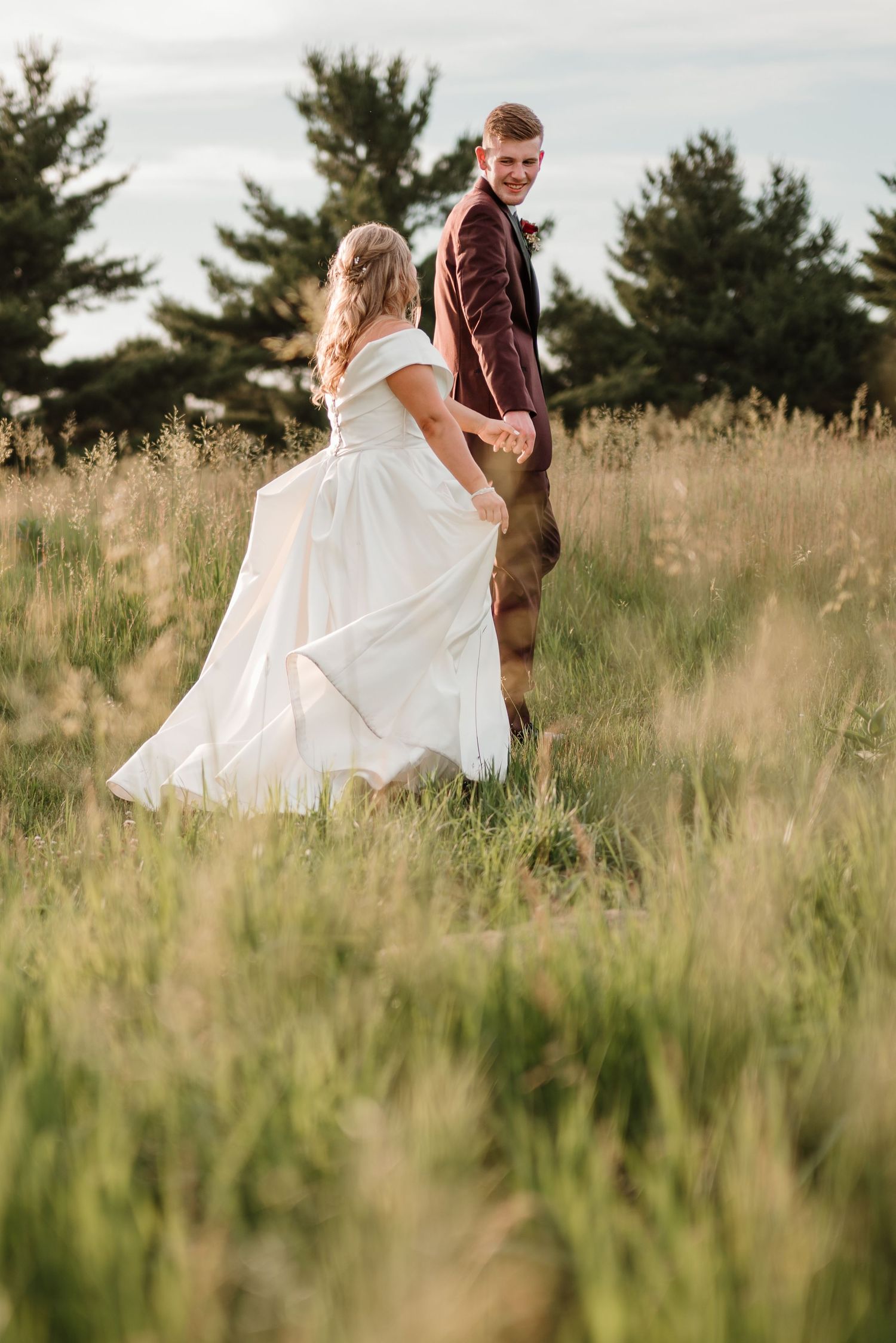 Couple walking through tall prairie grass in golden evening light at their June Iowa wedding