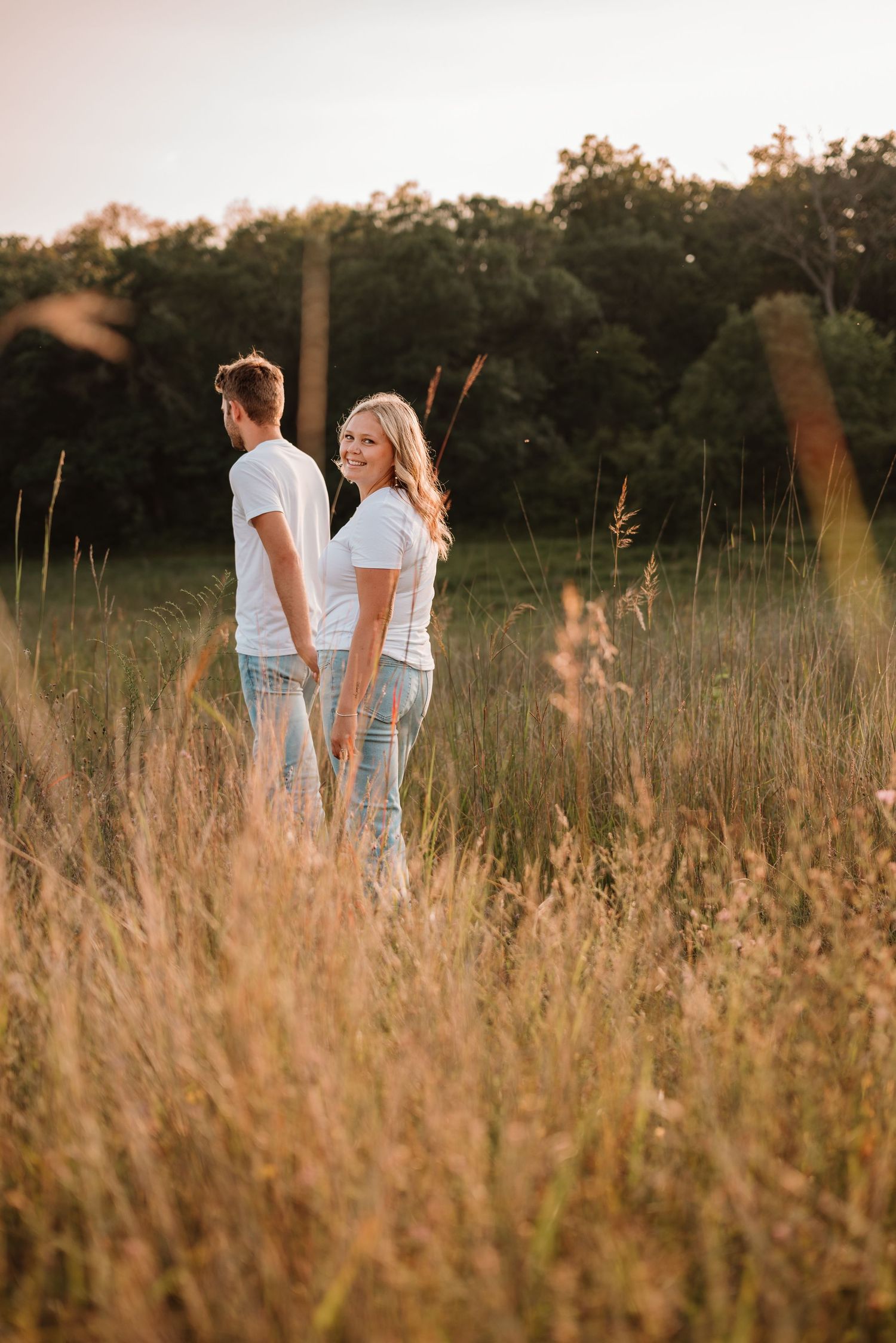 Couple walking hand in hand through a sunlit prairie in Minnesota