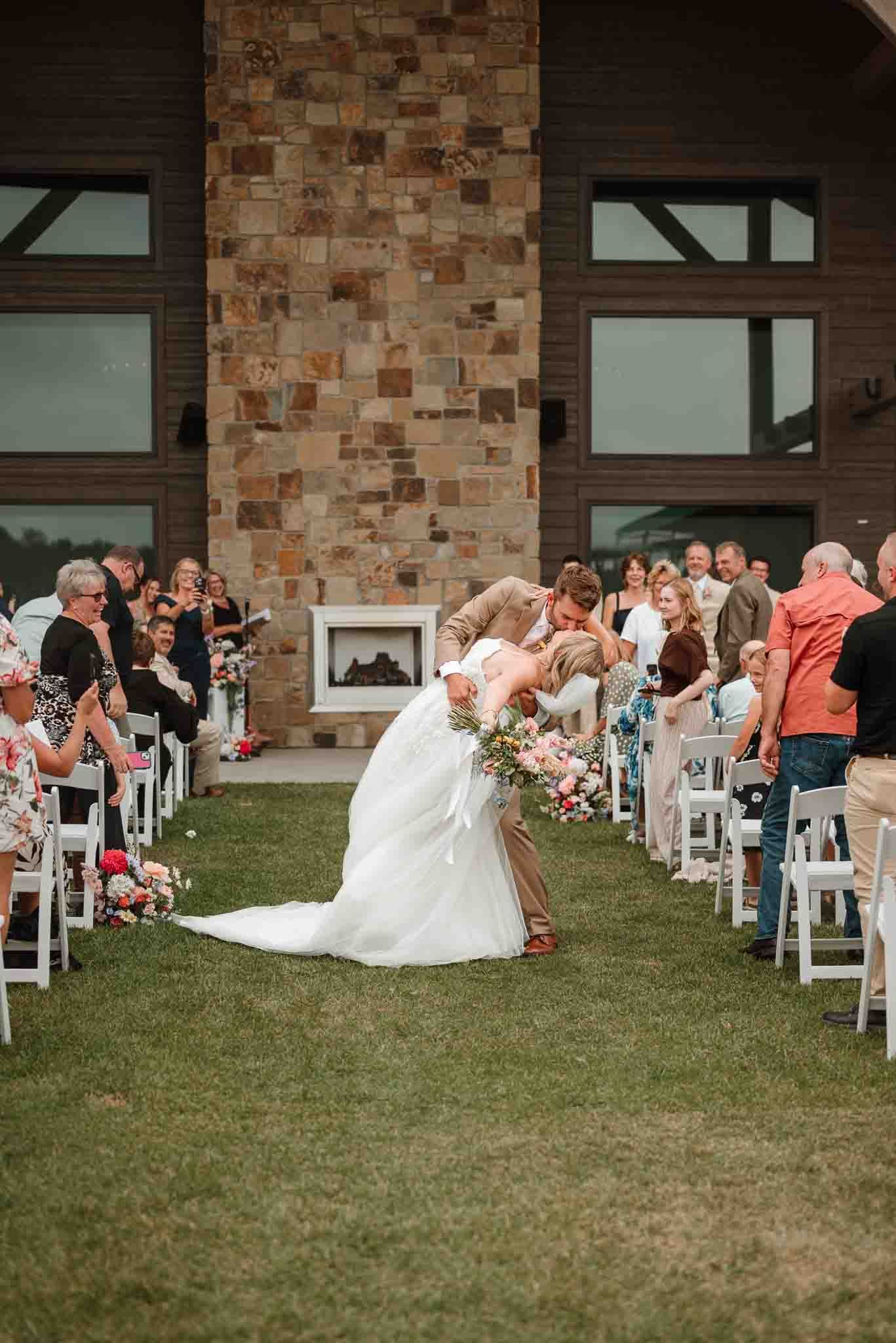 Bride and groom celebrating with a dip kiss while walking back down the aisle in Eau Claire
