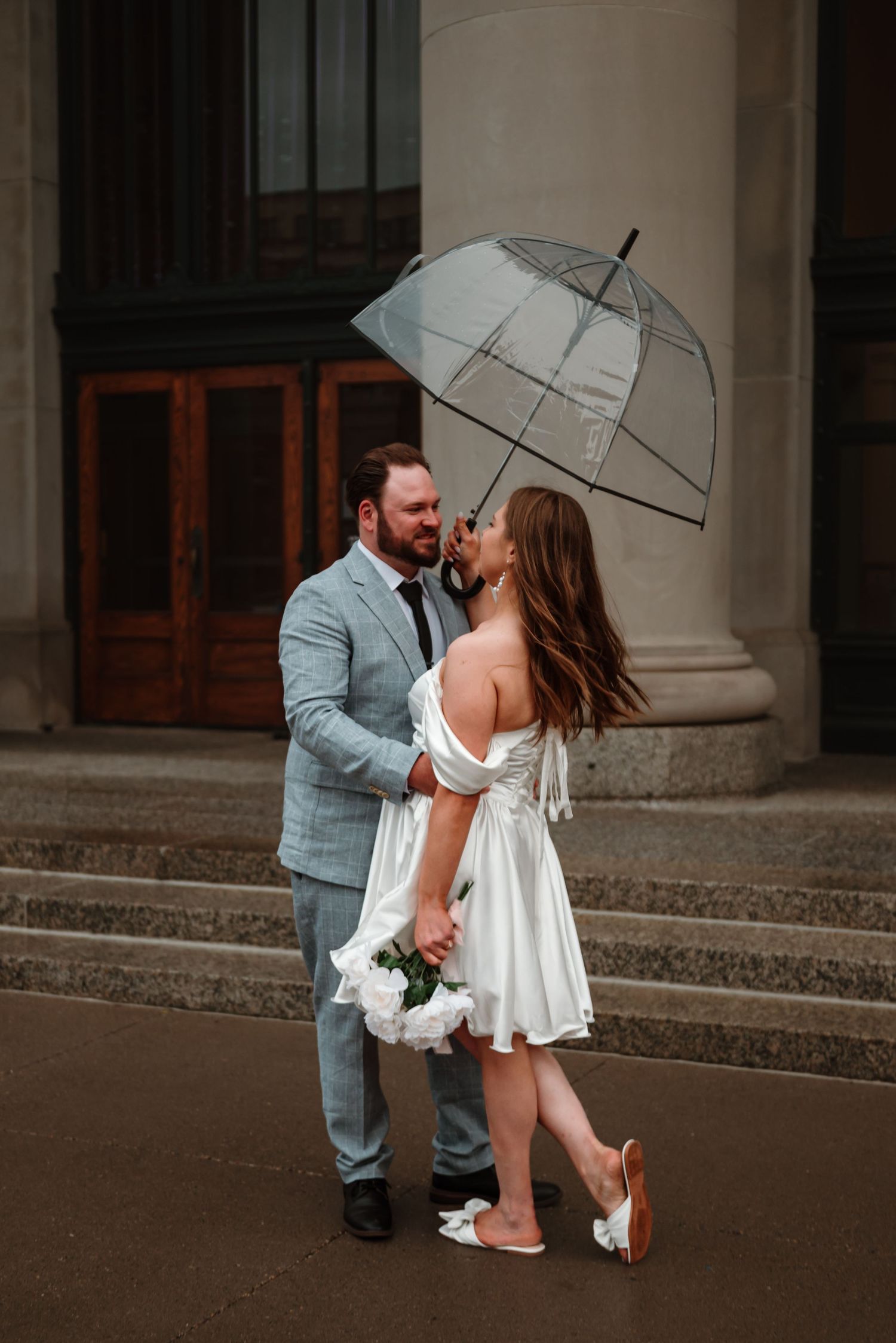 Couple laughing beneath an umbrella during their rainy engagement session in St Paul