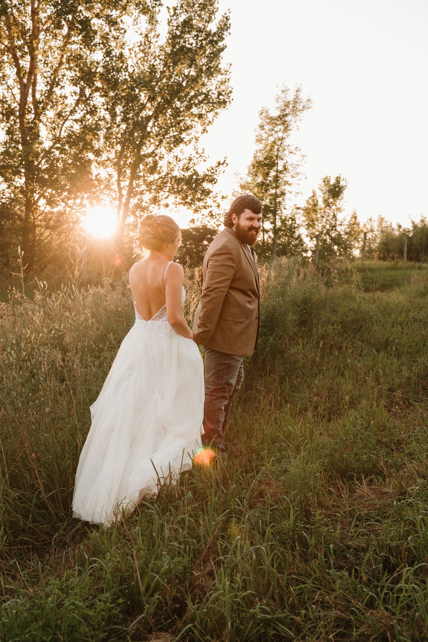 Couple walking holding hands in tall grassy field during sunset in Minnesota