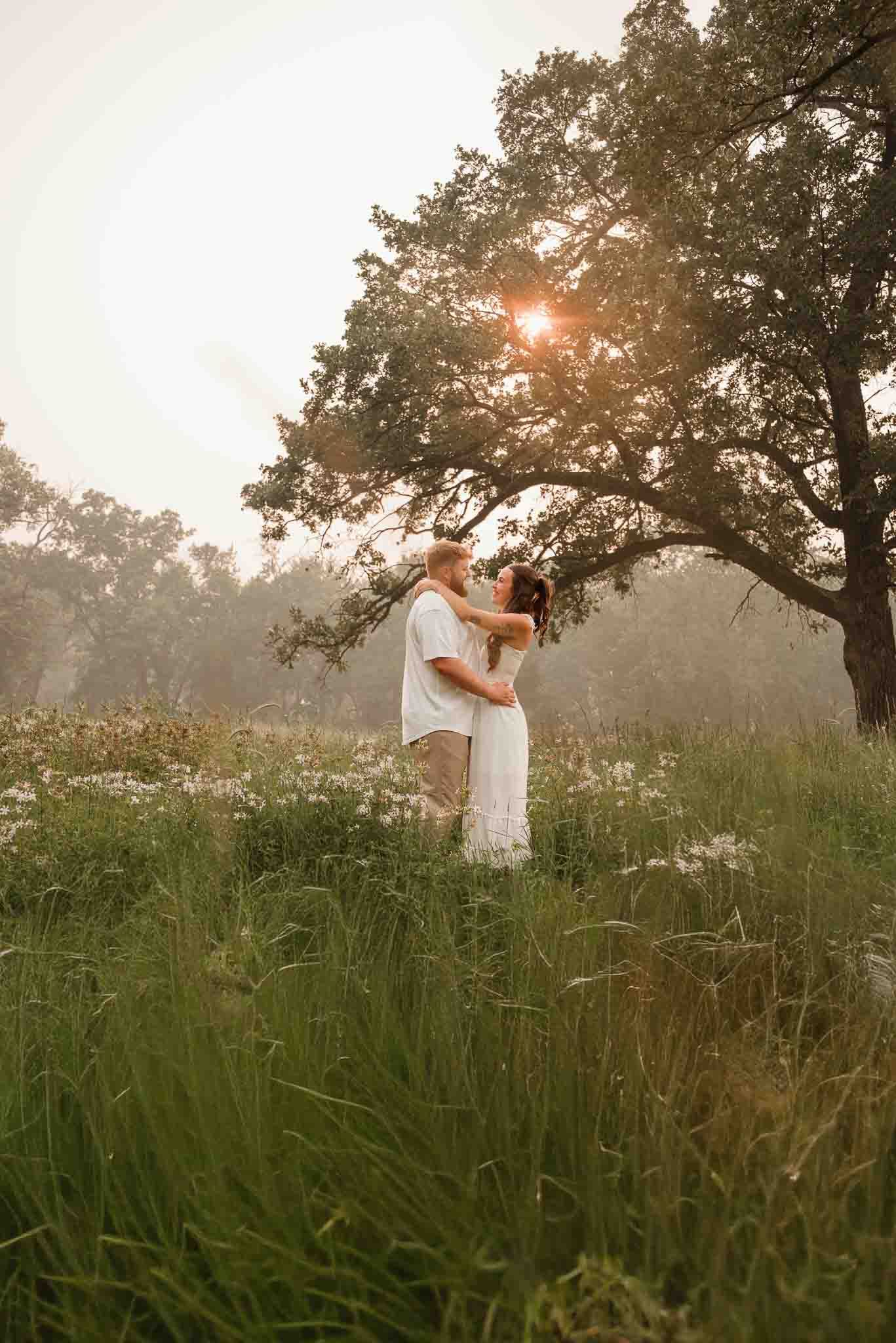 A couple in a field with the sun glinting through the trees in Minnesota