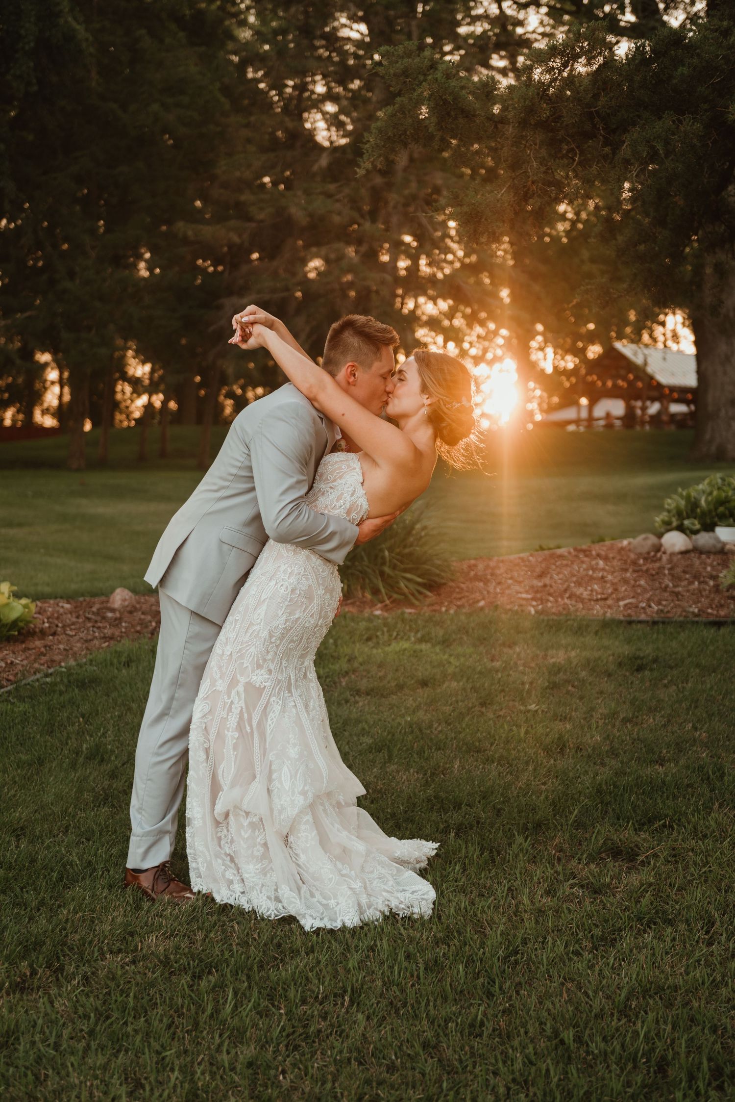 Couple dipping into a kiss with the setting sun through the trees behind at Northstar Farm in Minnesota
