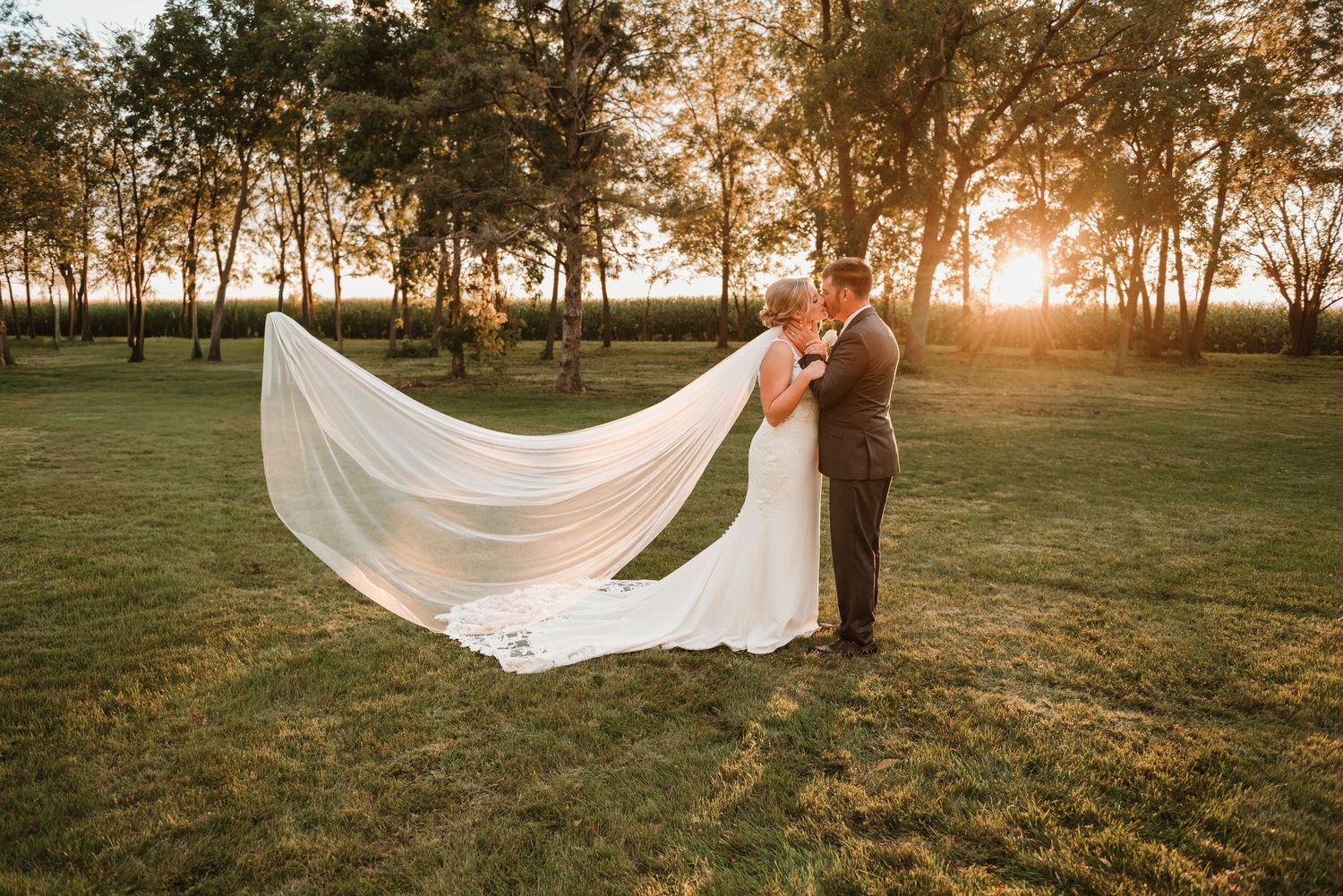 Couple sharing a quiet moment during sunset portraits with wind in her veil at their farm in Minnesota