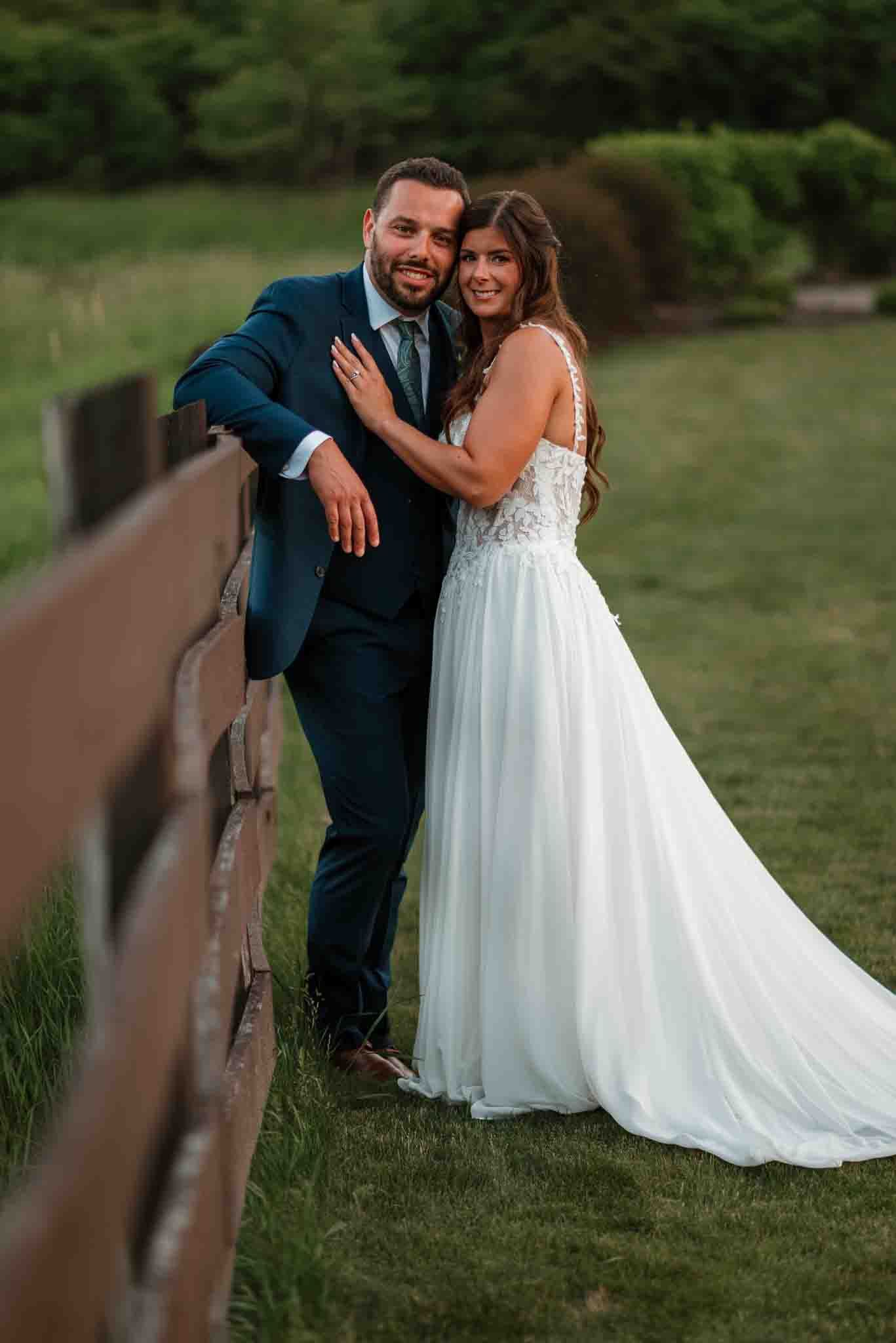 Newlyweds cuddling together as the sun sets behind a grassy Wisconsin field at Harvest Moon Pond