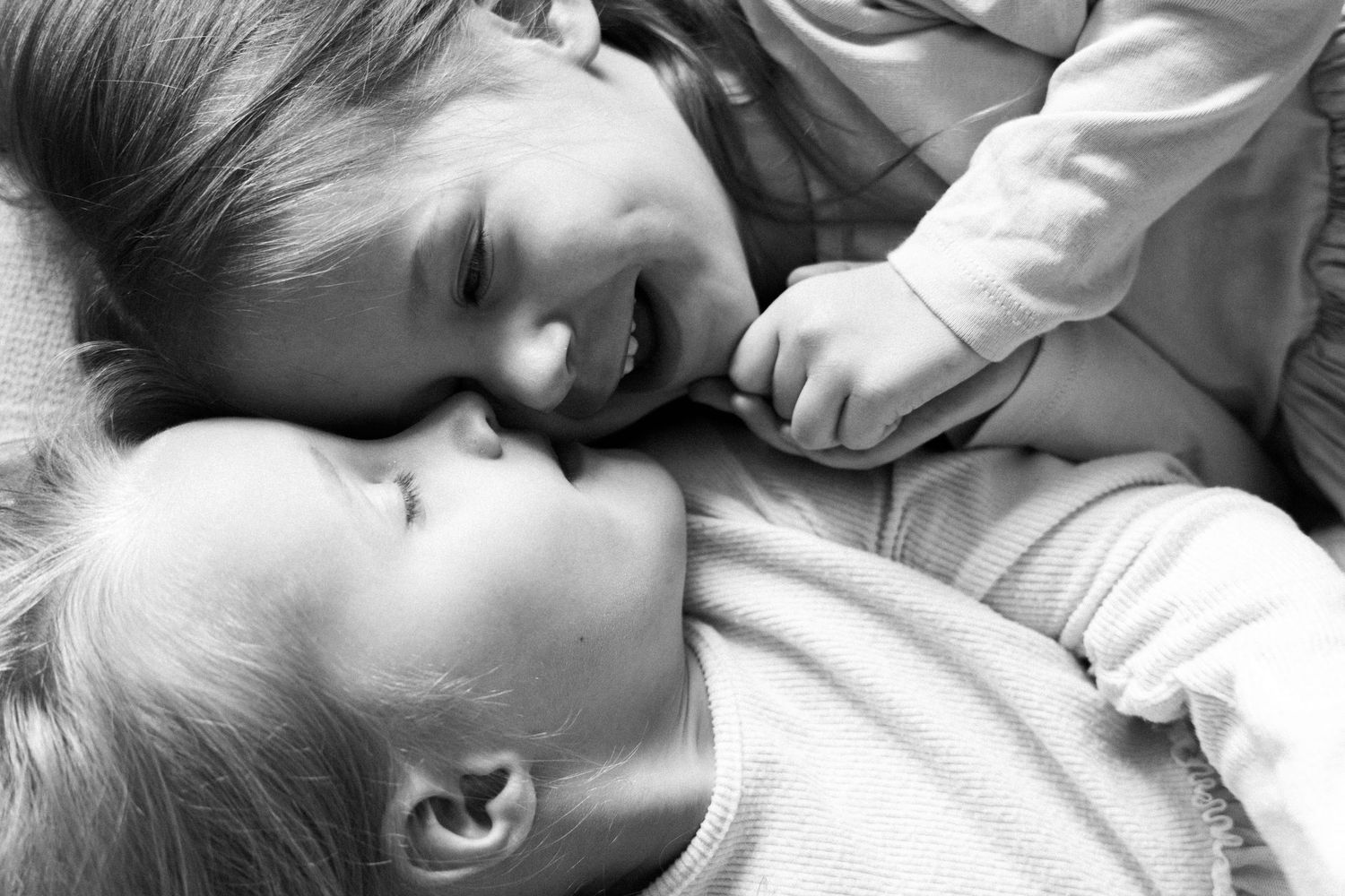 Black and white close-up of two young siblings lying face to face, smiling and bonding together.