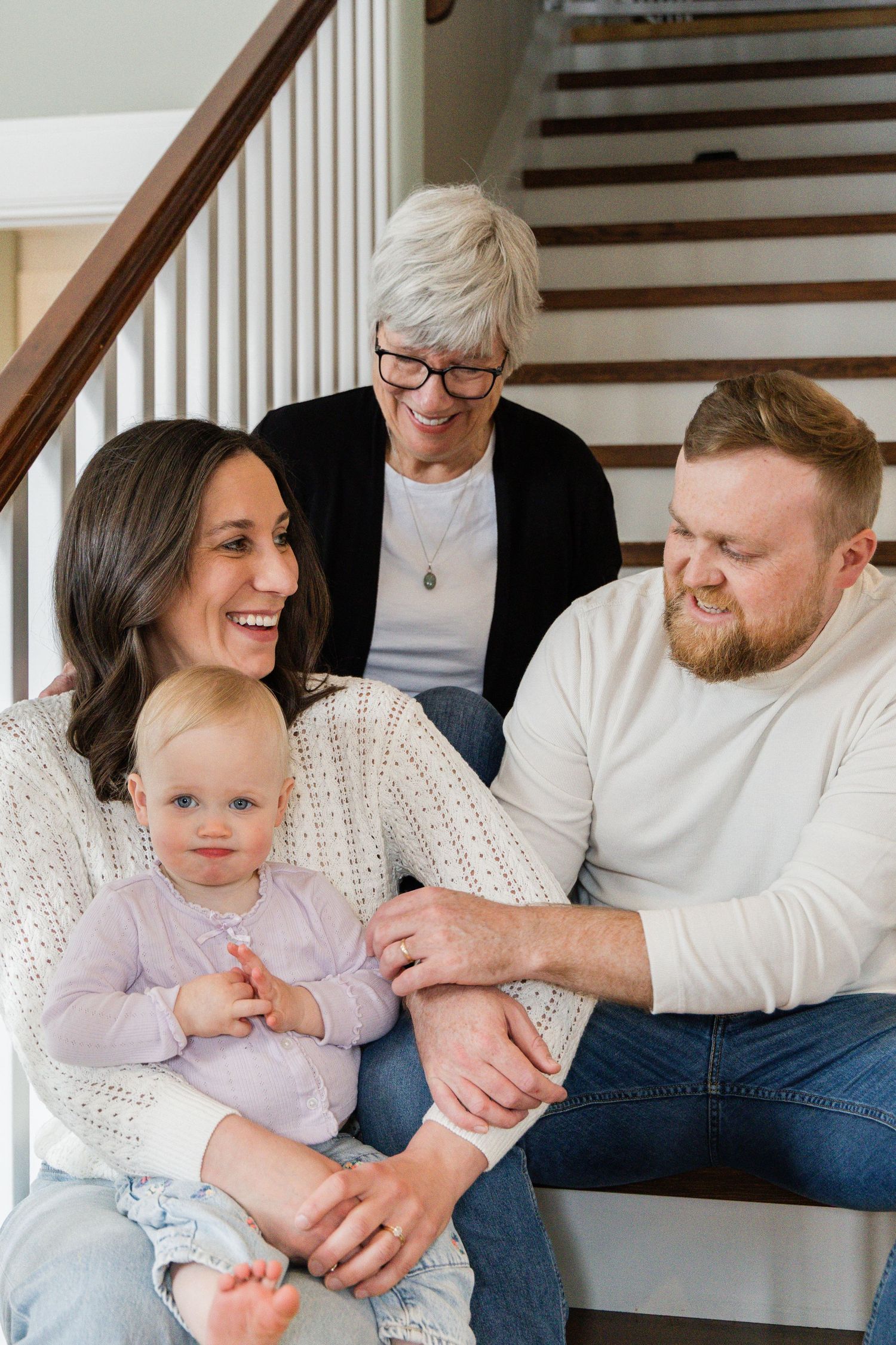 Happy three-generation family with grandma, parents, and blonde baby sitting on stairs.
