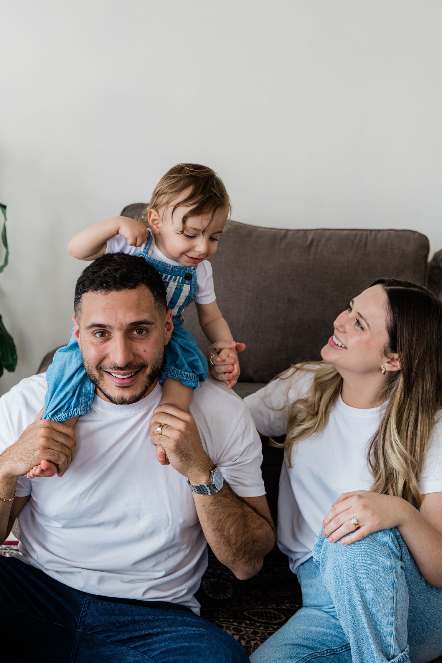 Joyful family portrait with dad carrying toddler on shoulders beside smiling mom.