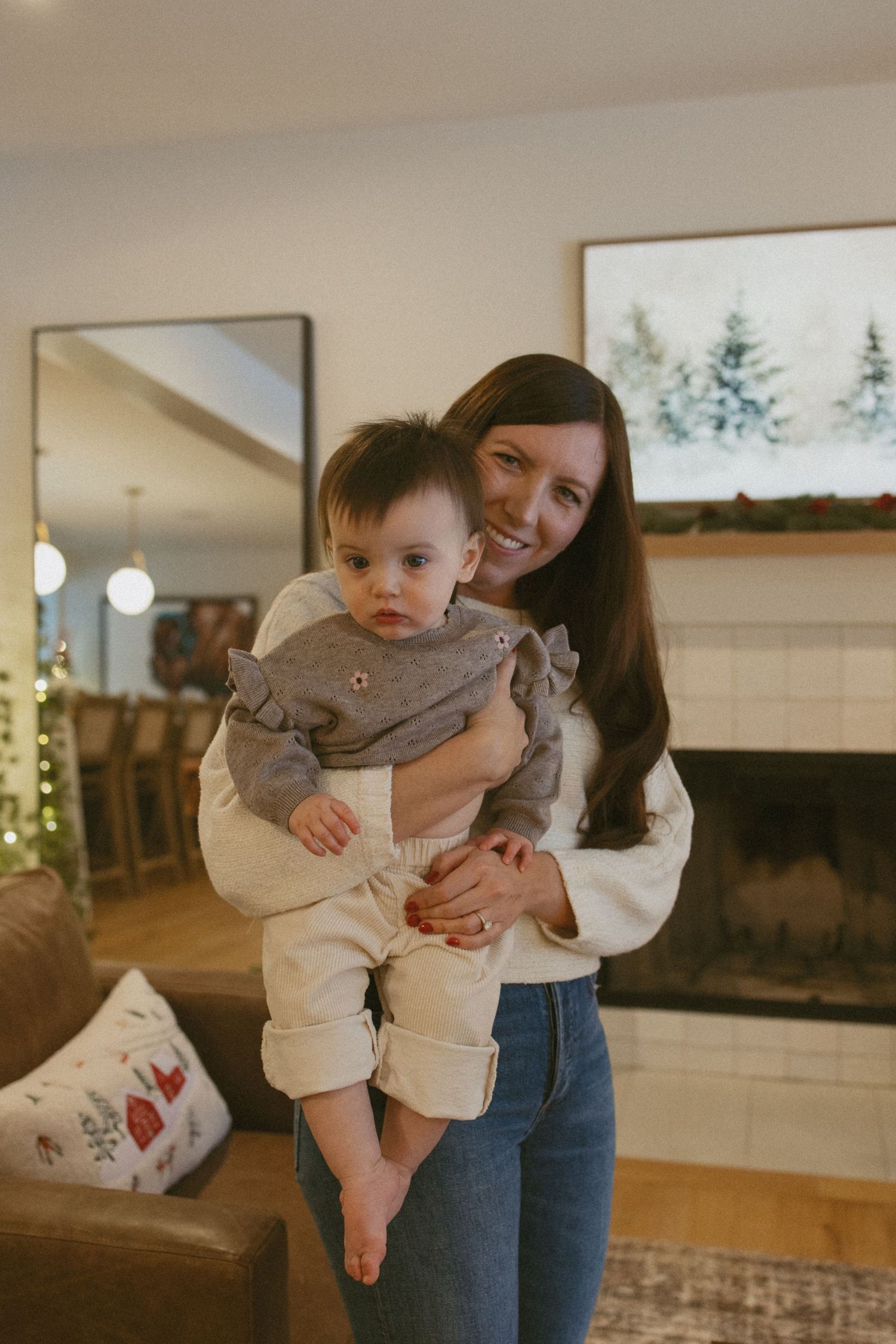 Smiling brunette mother holding her baby girl in a cozy Christmas decorated living room.