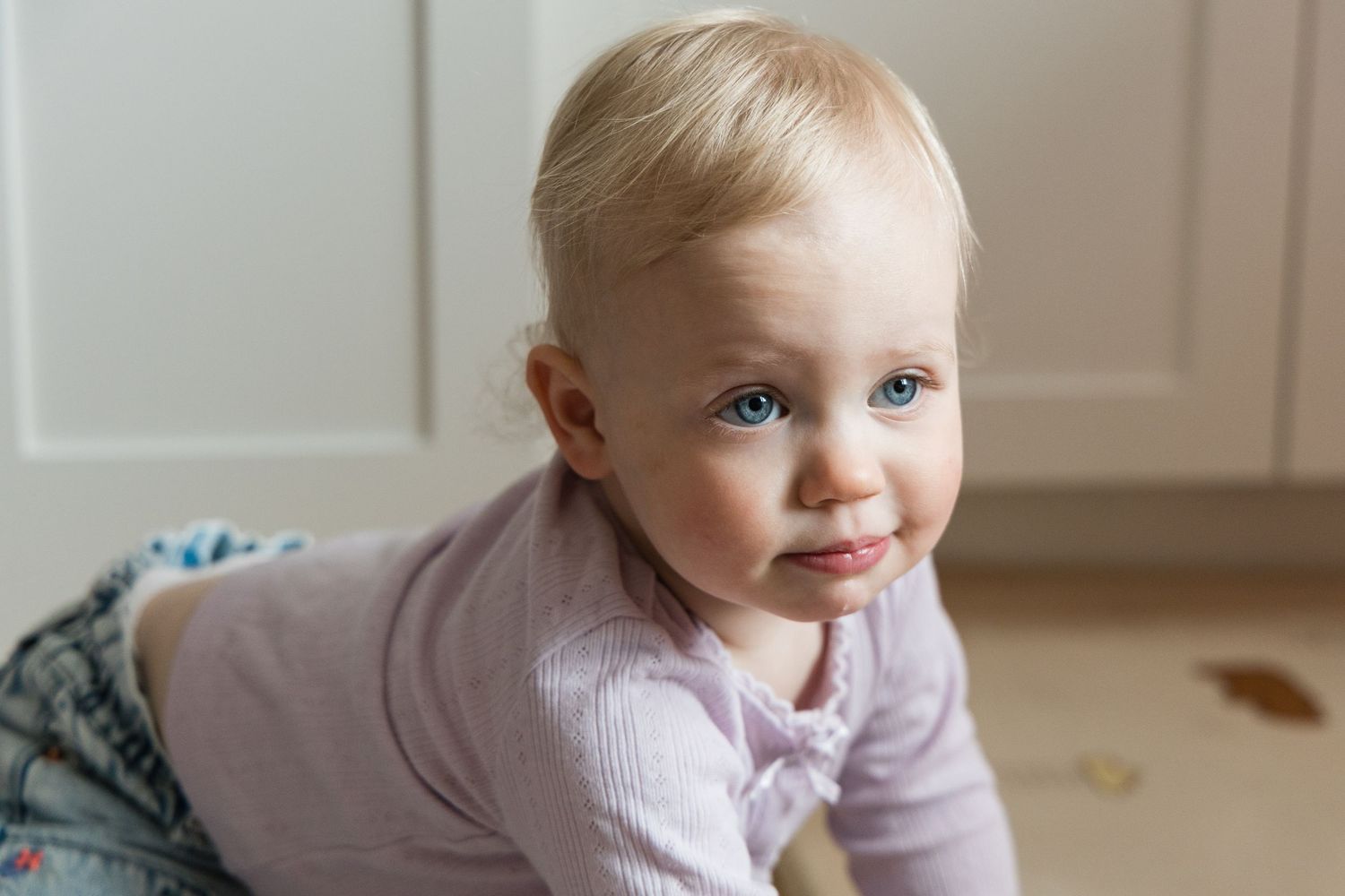 Cute blue-eyed blonde baby girl crawling on floor and looking at camera.
