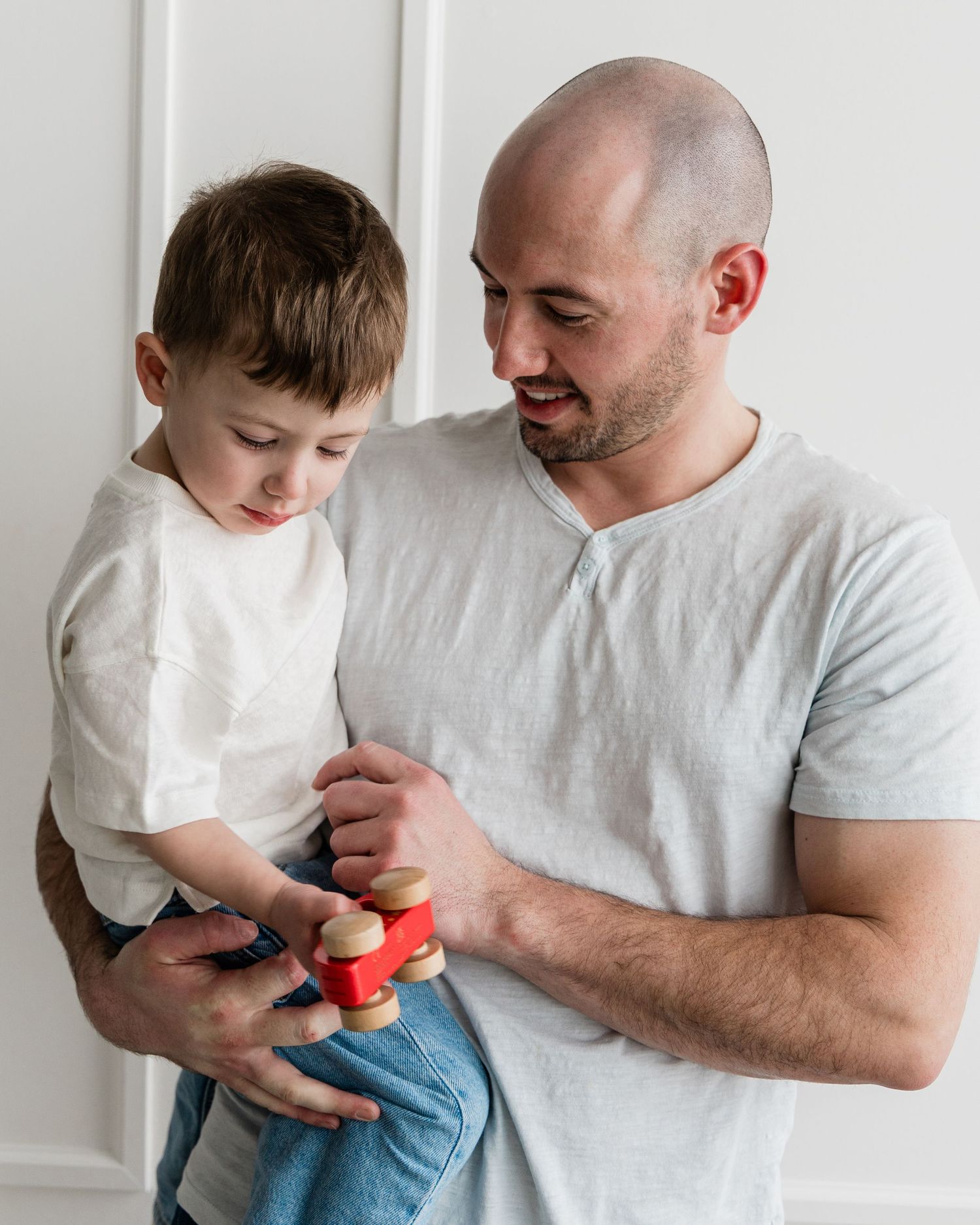 Bald father lovingly holding his toddler son while they play together with a colorful wooden toy.