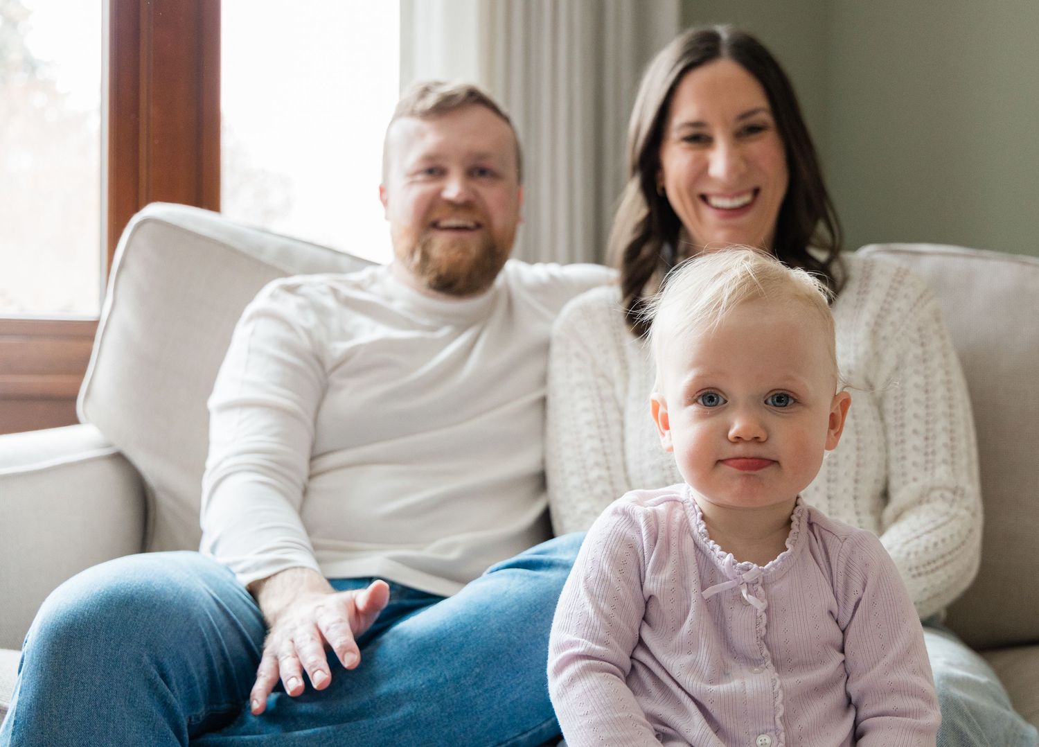 Happy family portrait with parents and toddler sitting on couch at home.
