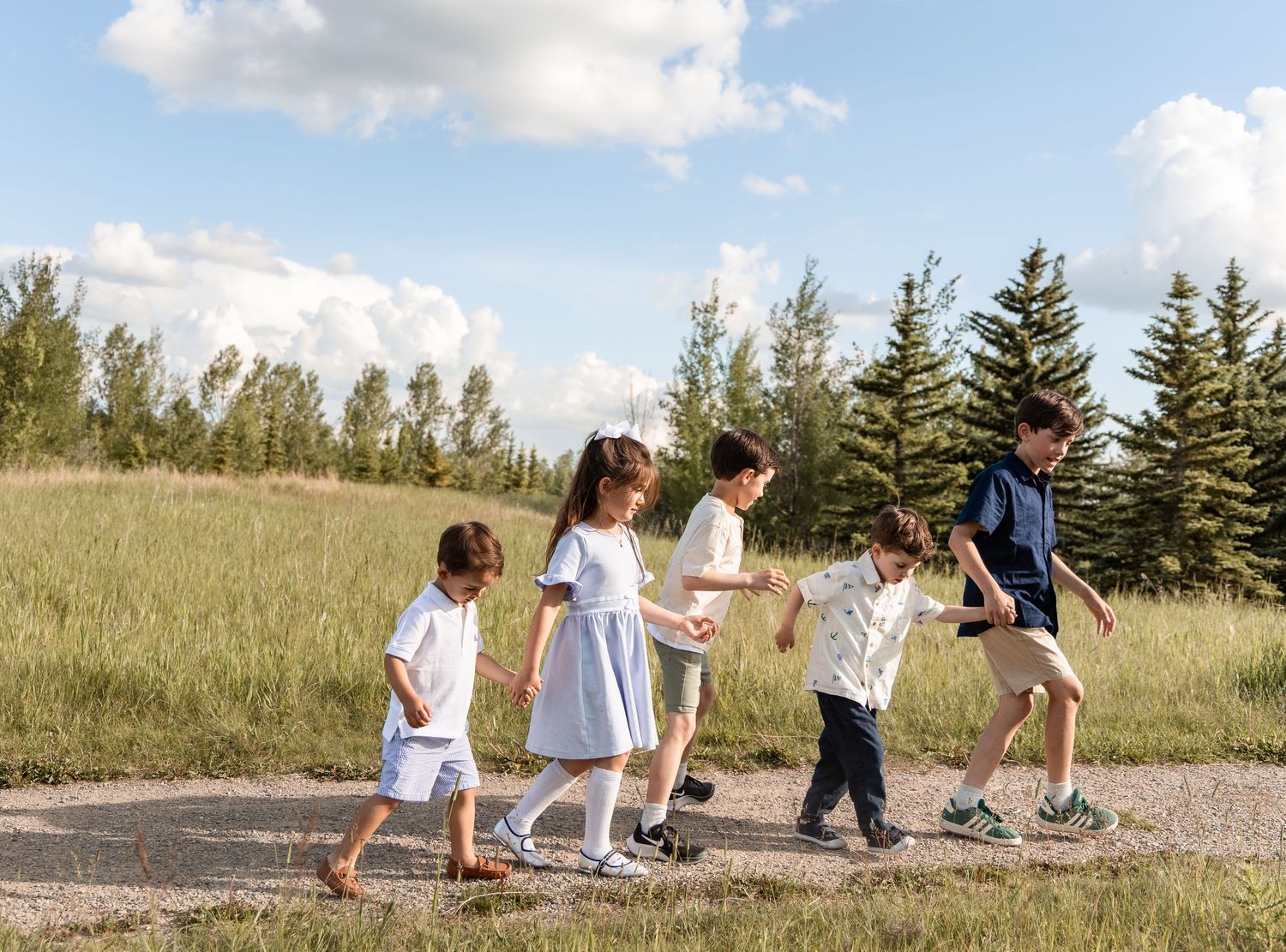 Group of five children walking together on a path with trees in background.