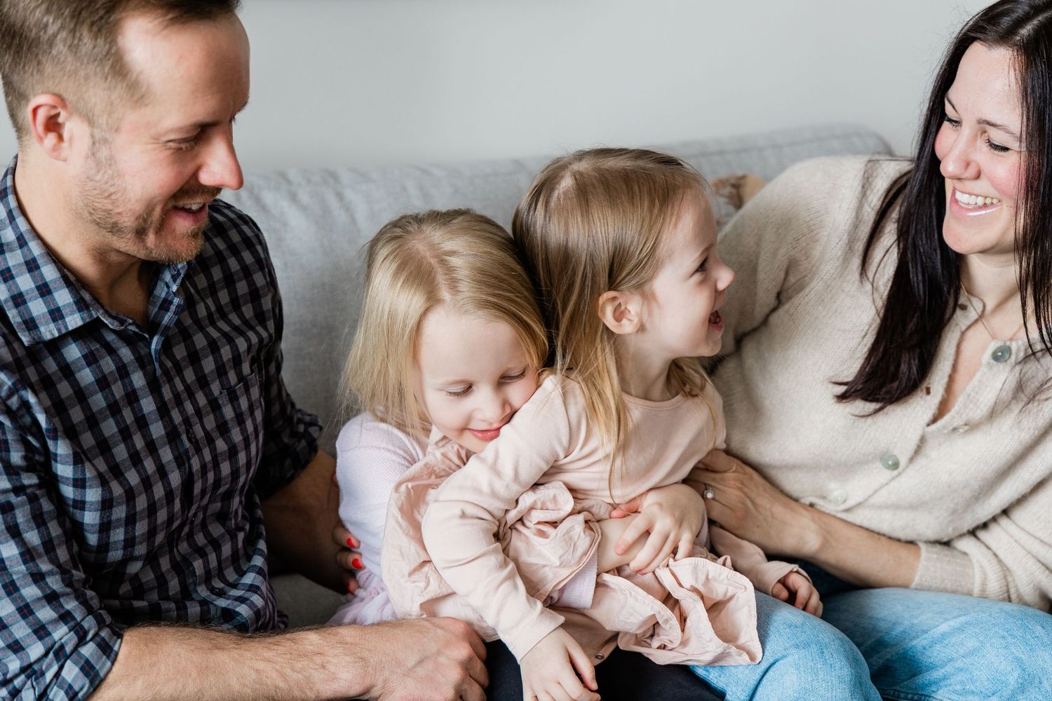 Happy family of four with two young daughters sharing a joyful moment together on a cozy sofa.