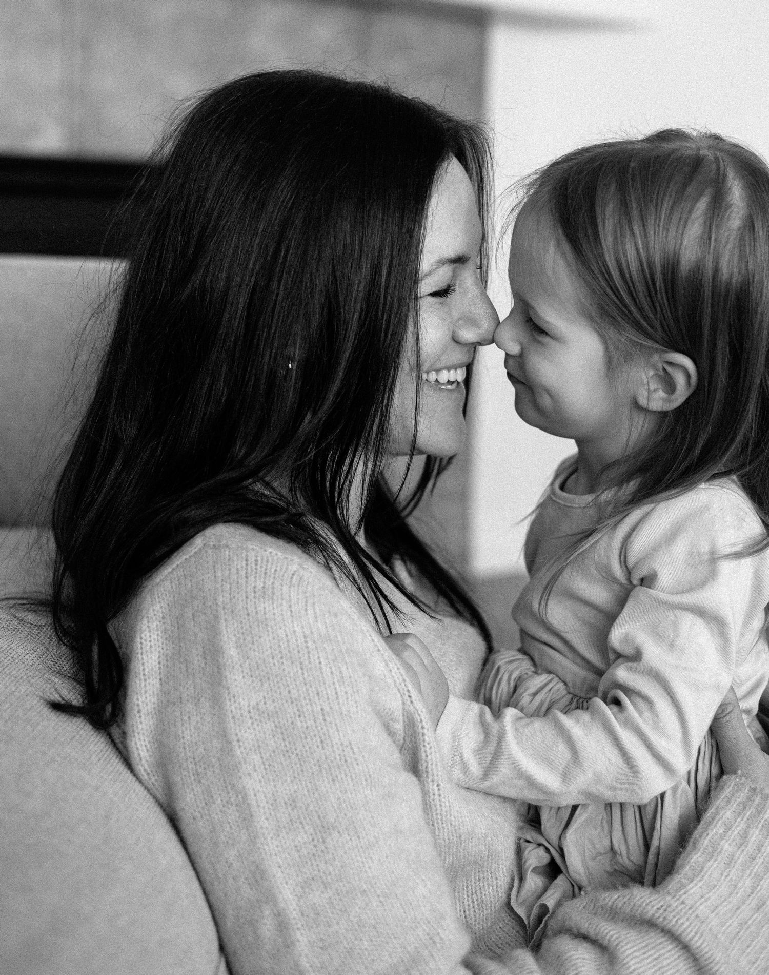 Black and white photo of a smiling mother and young daughter touching foreheads in a tender, loving moment.