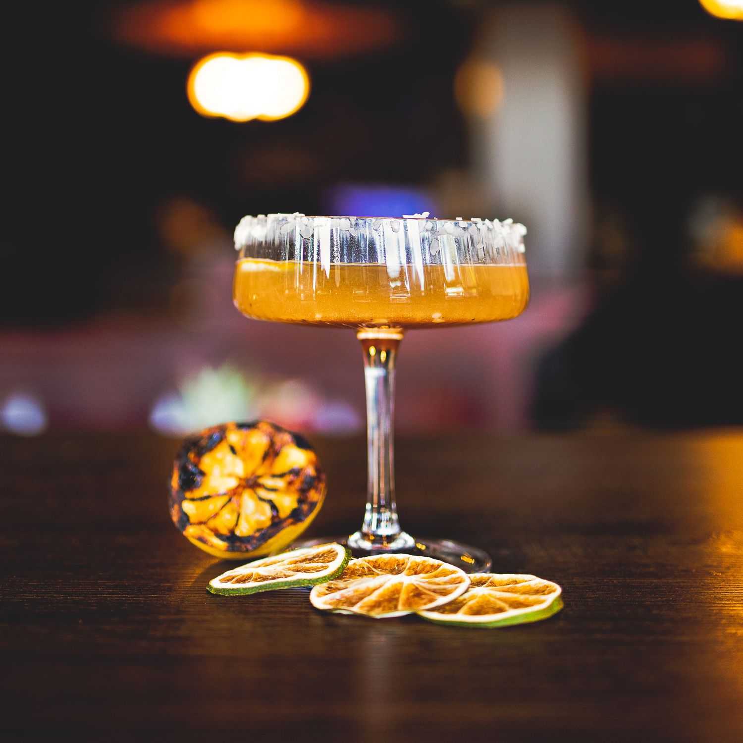 Professional food photography of an orange cocktail in a coupe glass garnished with dried citrus slices on a bar counter.