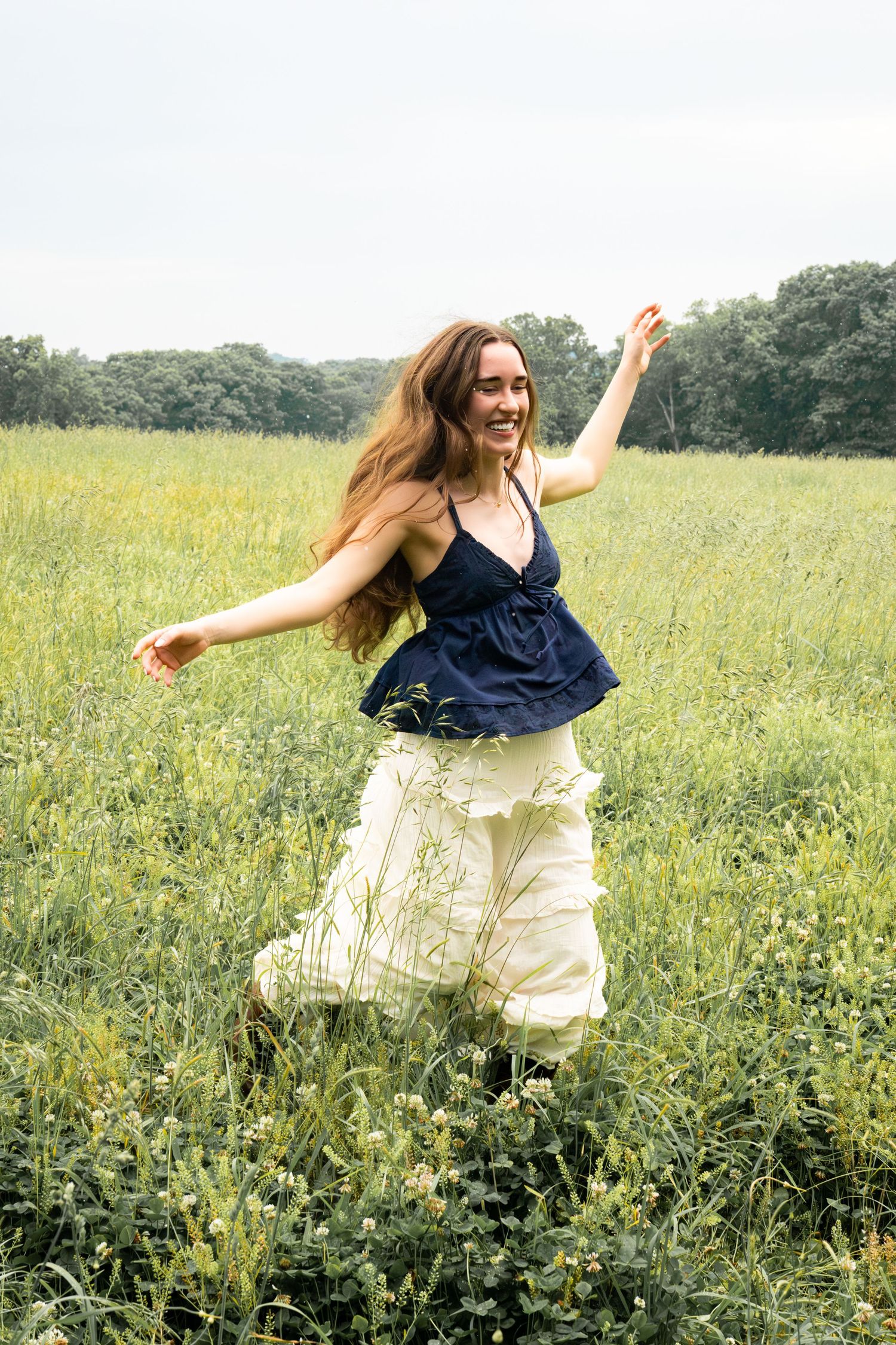 Joyful young woman in navy top and white skirt dancing freely in a wildflower meadow.